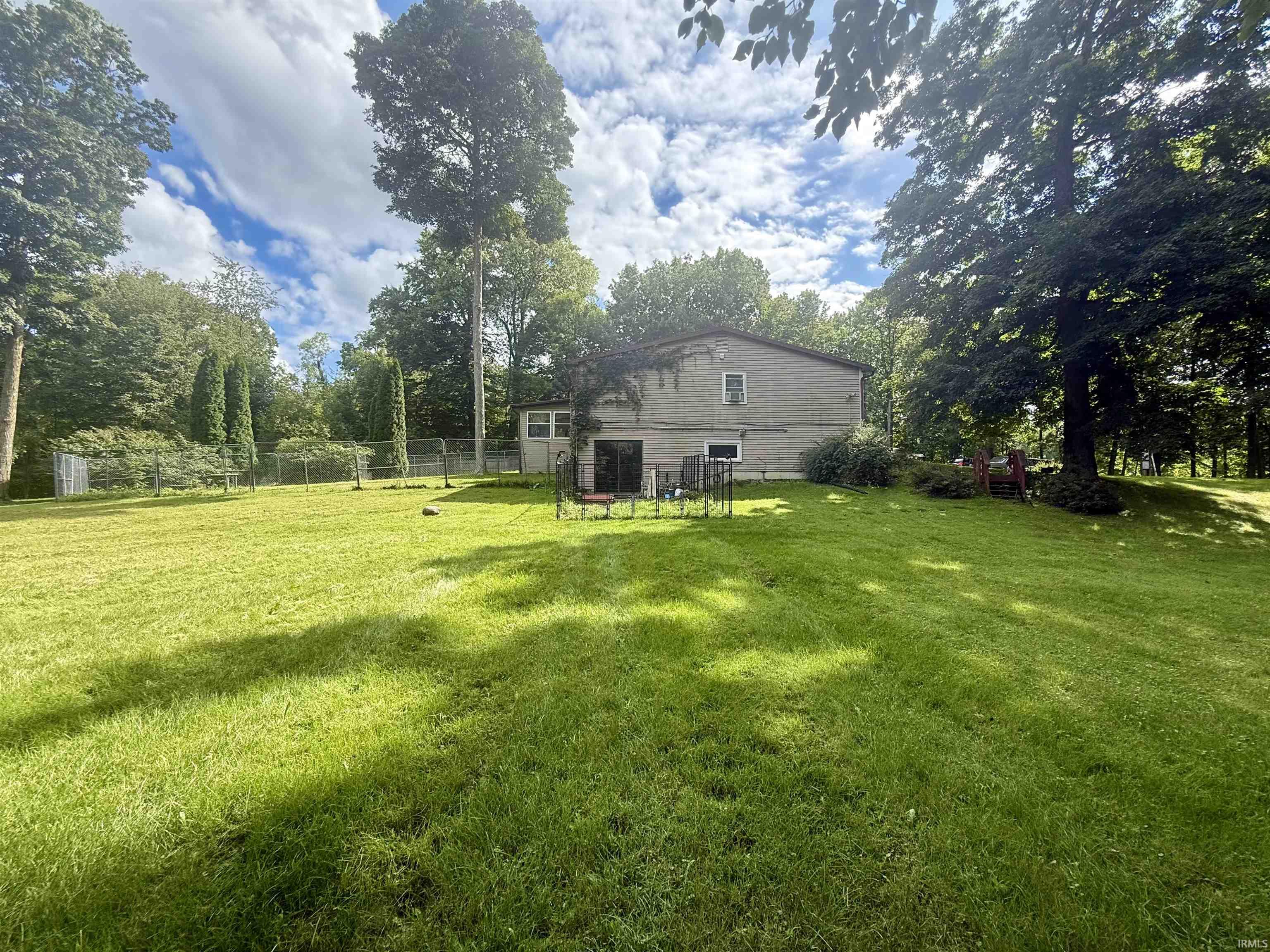 Expansive green lawn framed by mature trees, featuring a detached storage shed and partial fencing