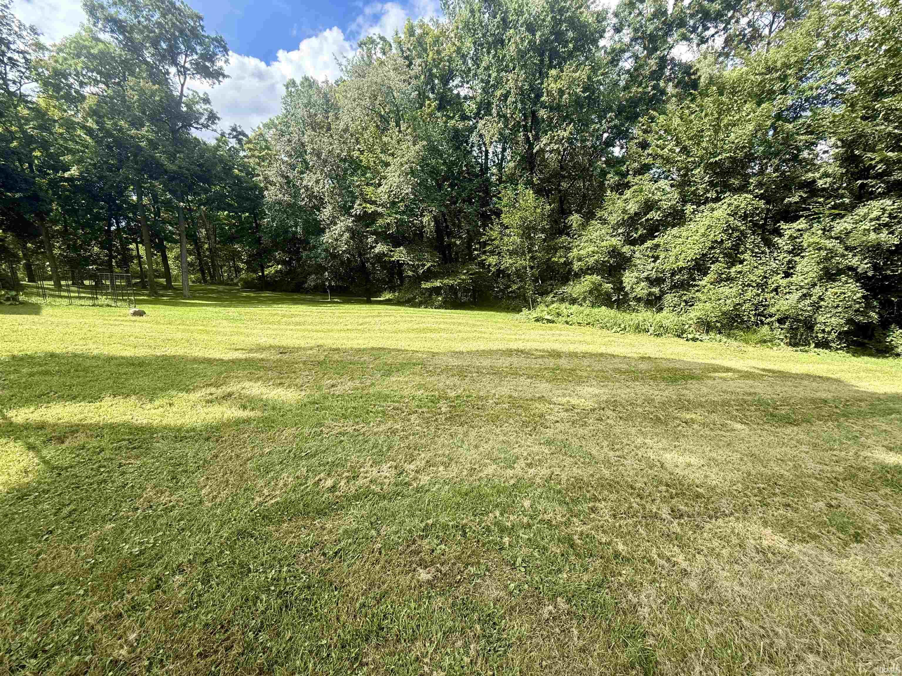 Expansive lawn area featuring mature trees and established perimeter fencing