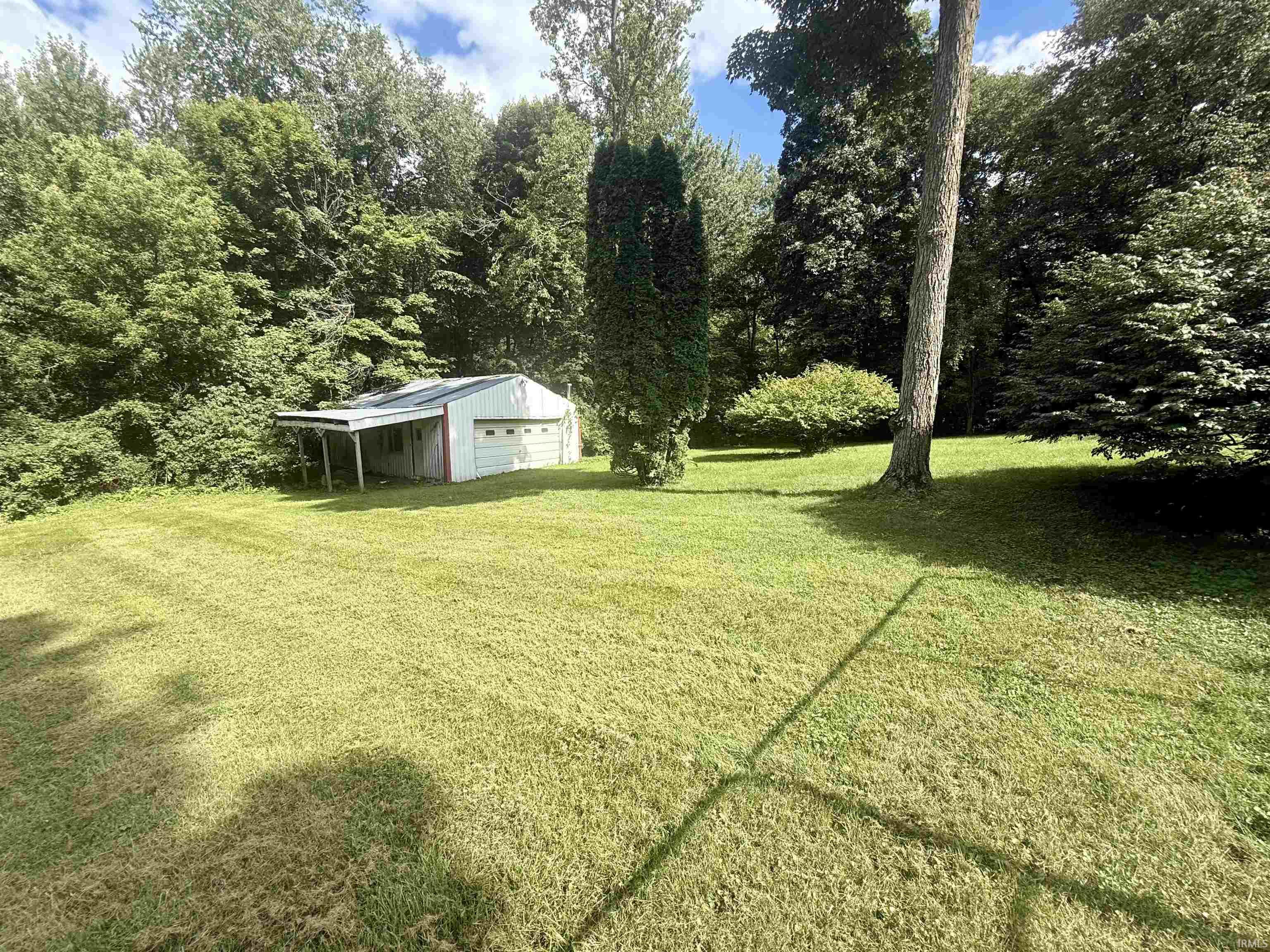 Detached garage structure with a single bay, covered side area, and surrounding mature trees