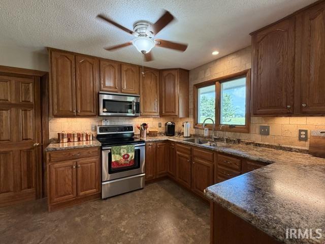 Kitchen featuring wood cabinetry, stainless steel appliances, granite-style countertops, tile backsplash, and a ceiling fan with integrated lighting