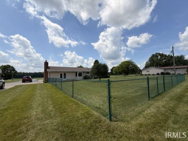 Expansive green lawn enclosed by a chain-link fence, featuring a paved driveway and mature trees