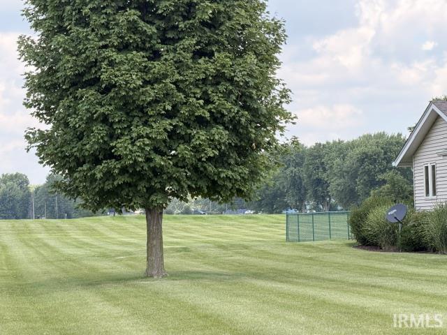 Expansive green lawn with striped mowing patterns, mature shade tree, and partial view of a light-colored siding structure