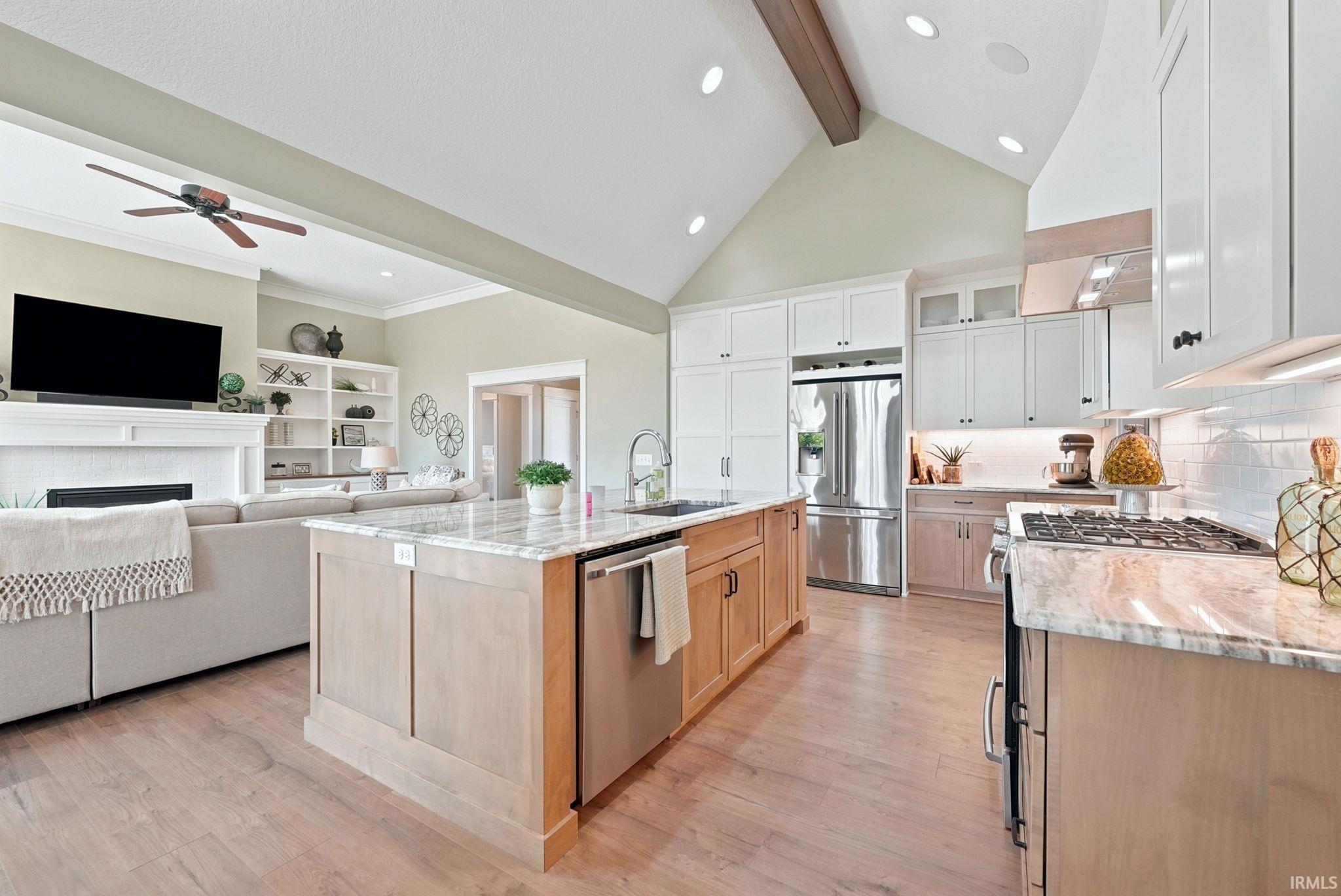 Open-concept kitchen featuring wood-finish flooring, a central island with integrated sink, stainless steel appliances, and two-tone cabinetry with under-cabinet lighting