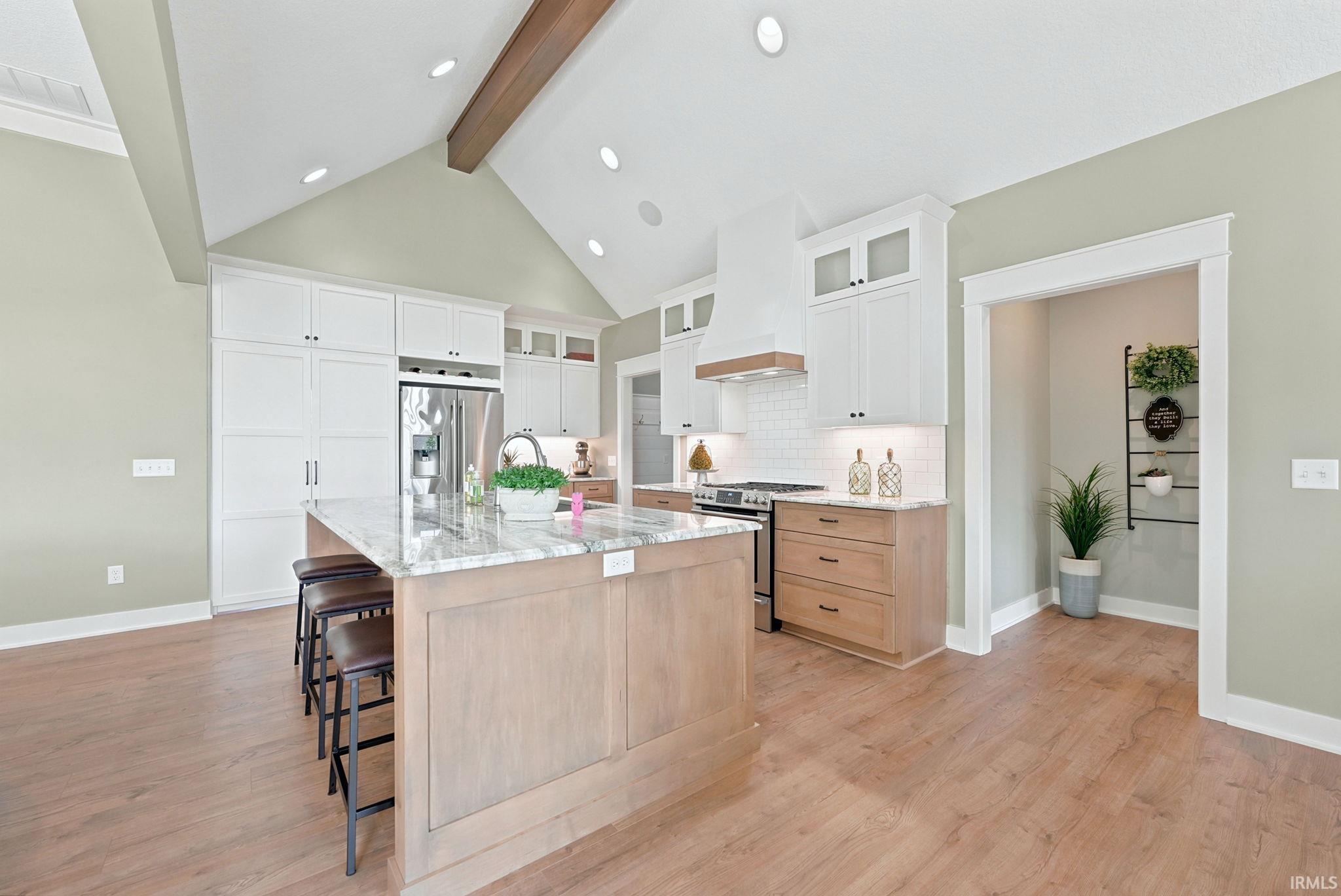 Gourmet kitchen featuring a large central island with seating, stainless steel appliances, a paneled refrigerator, and a vaulted ceiling with a wood beam accent