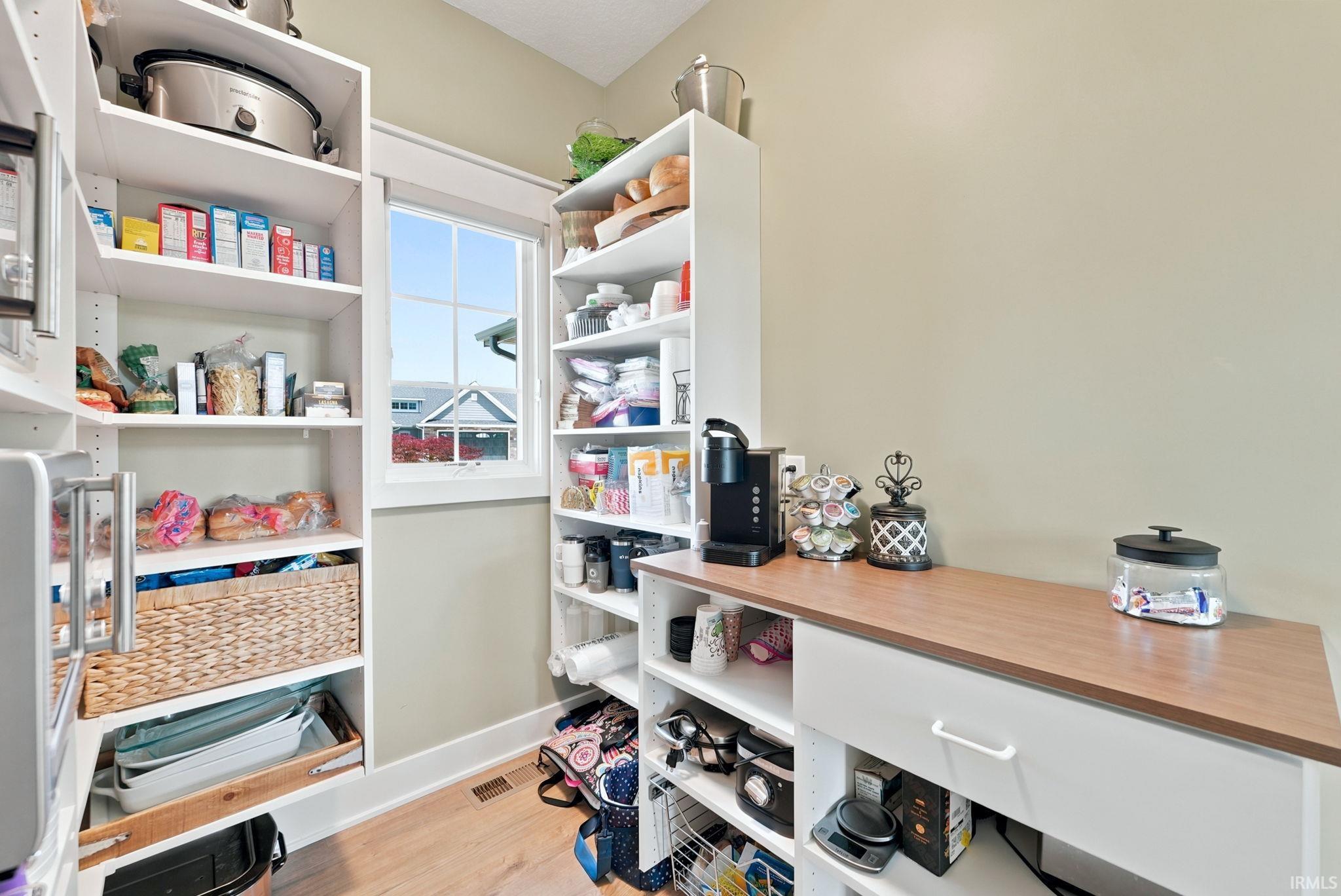 Walk-in pantry featuring extensive white built-in shelving, wood-finish countertop, and wood-finish flooring