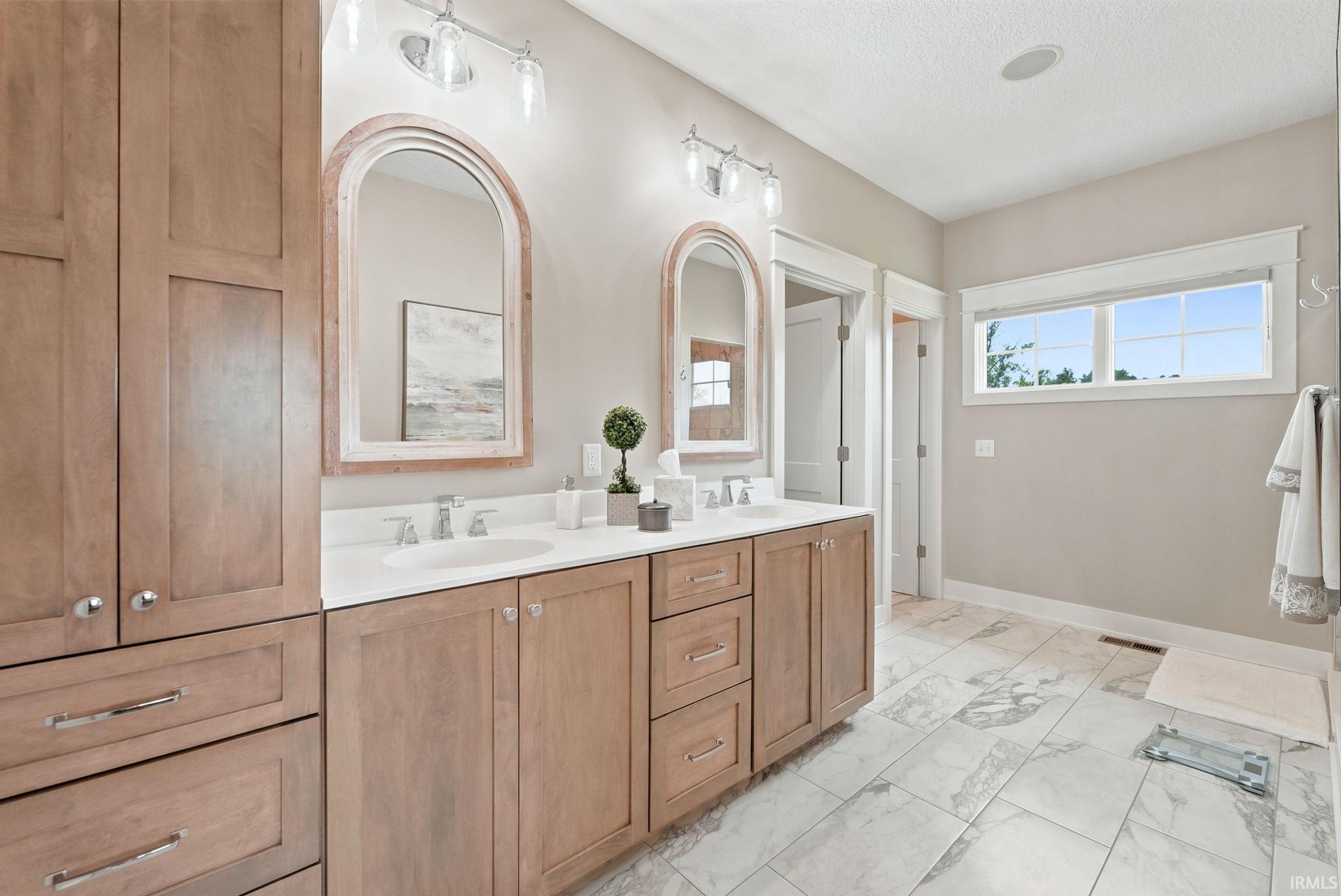Bathroom with dual-sink vanity, light wood-finish cabinetry, and arched mirrors