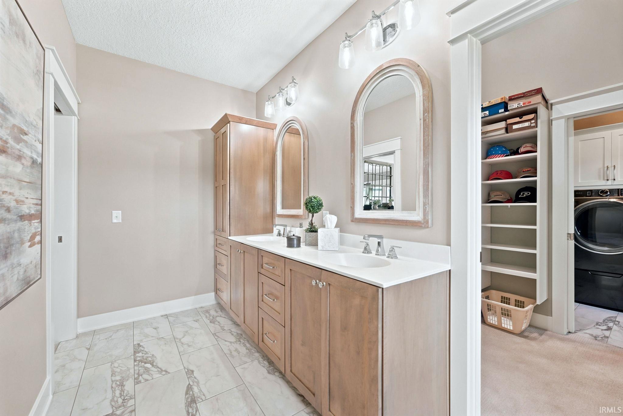 Bathroom featuring dual light wood-finish vanities with undermount sinks, white countertops, and arched framed mirrors