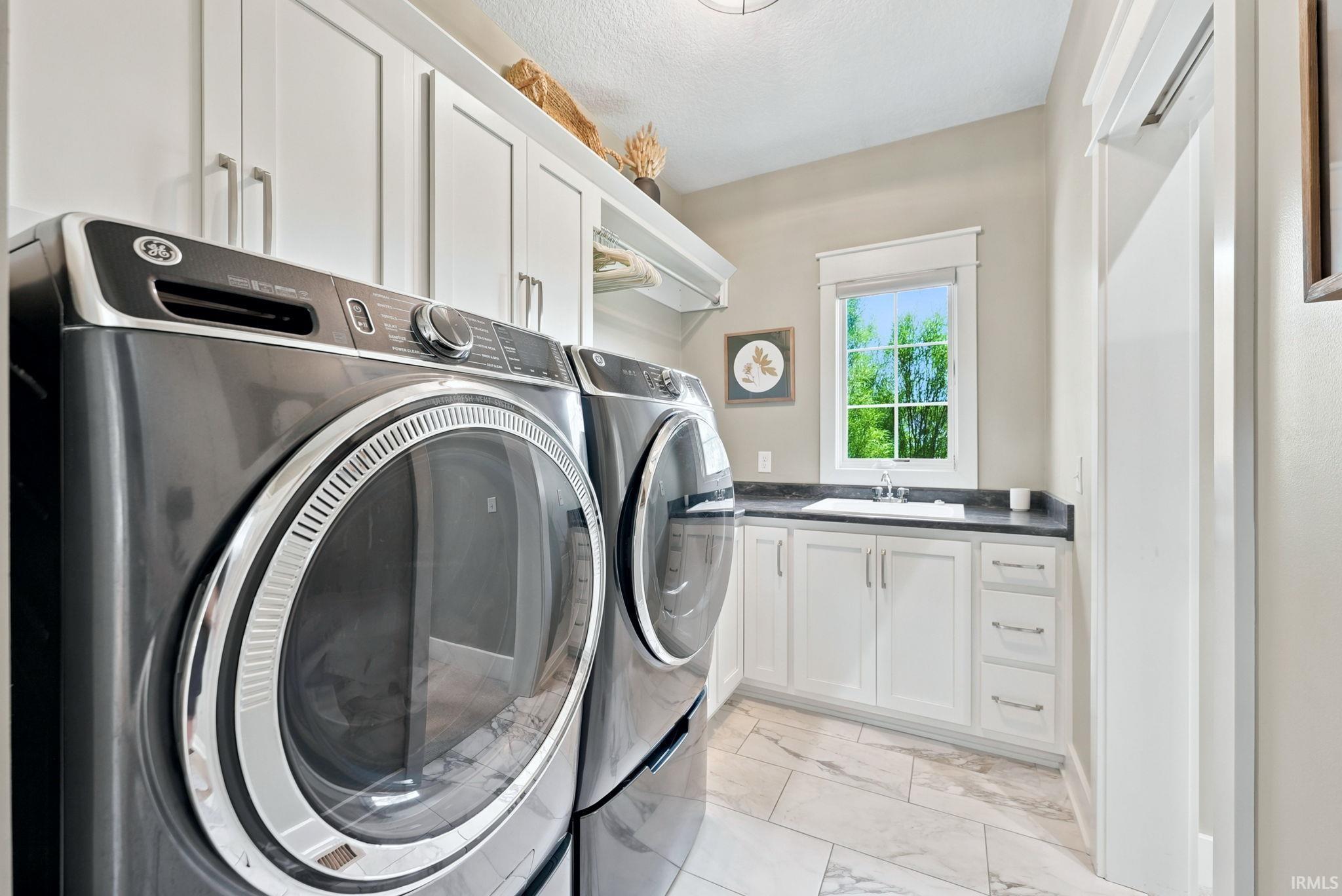 Laundry area featuring floor-to-ceiling white cabinetry, a built-in sink with dark countertops, and large format tile flooring
