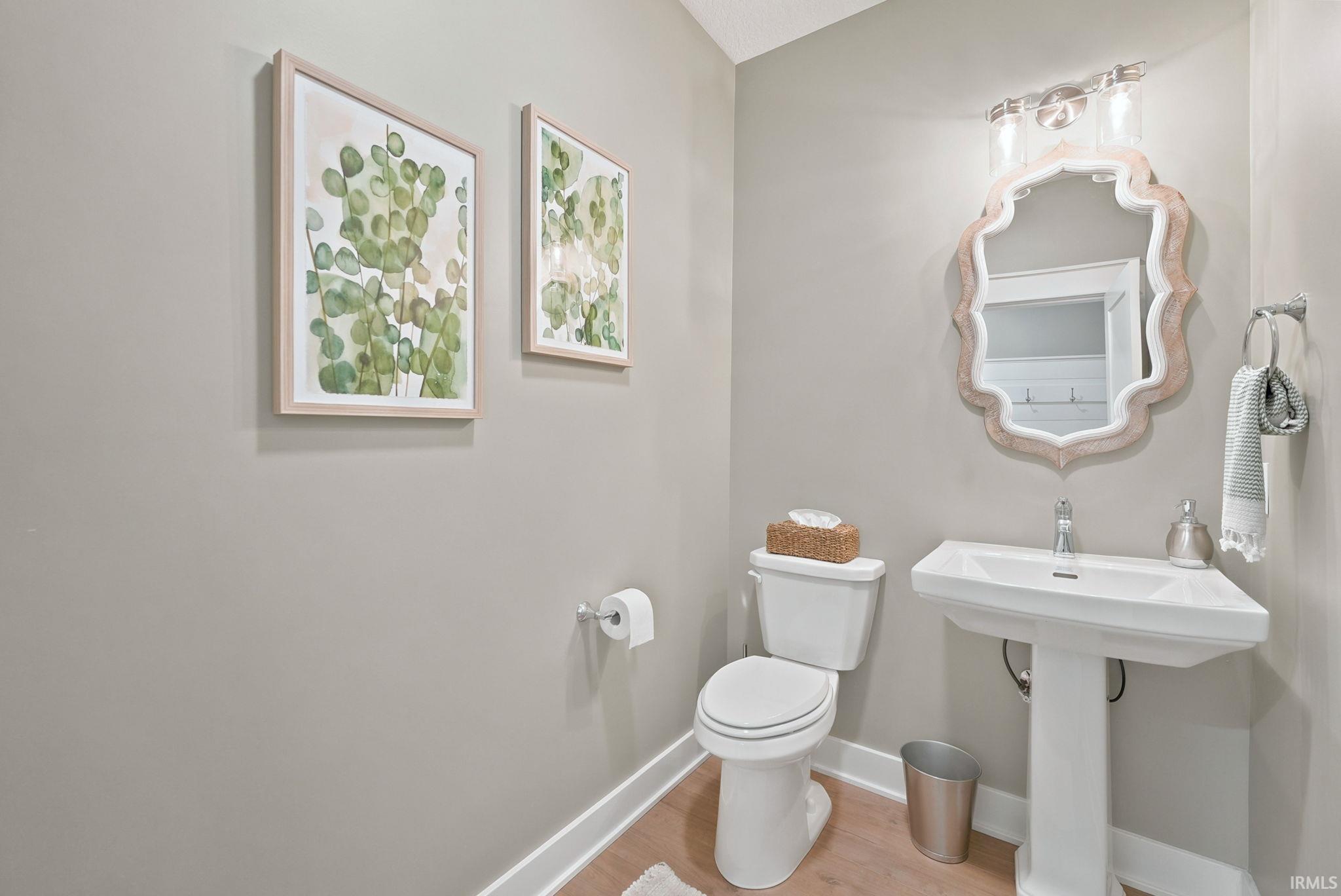 Powder room featuring a white pedestal sink, decorative wall mirror, and wood-finish flooring