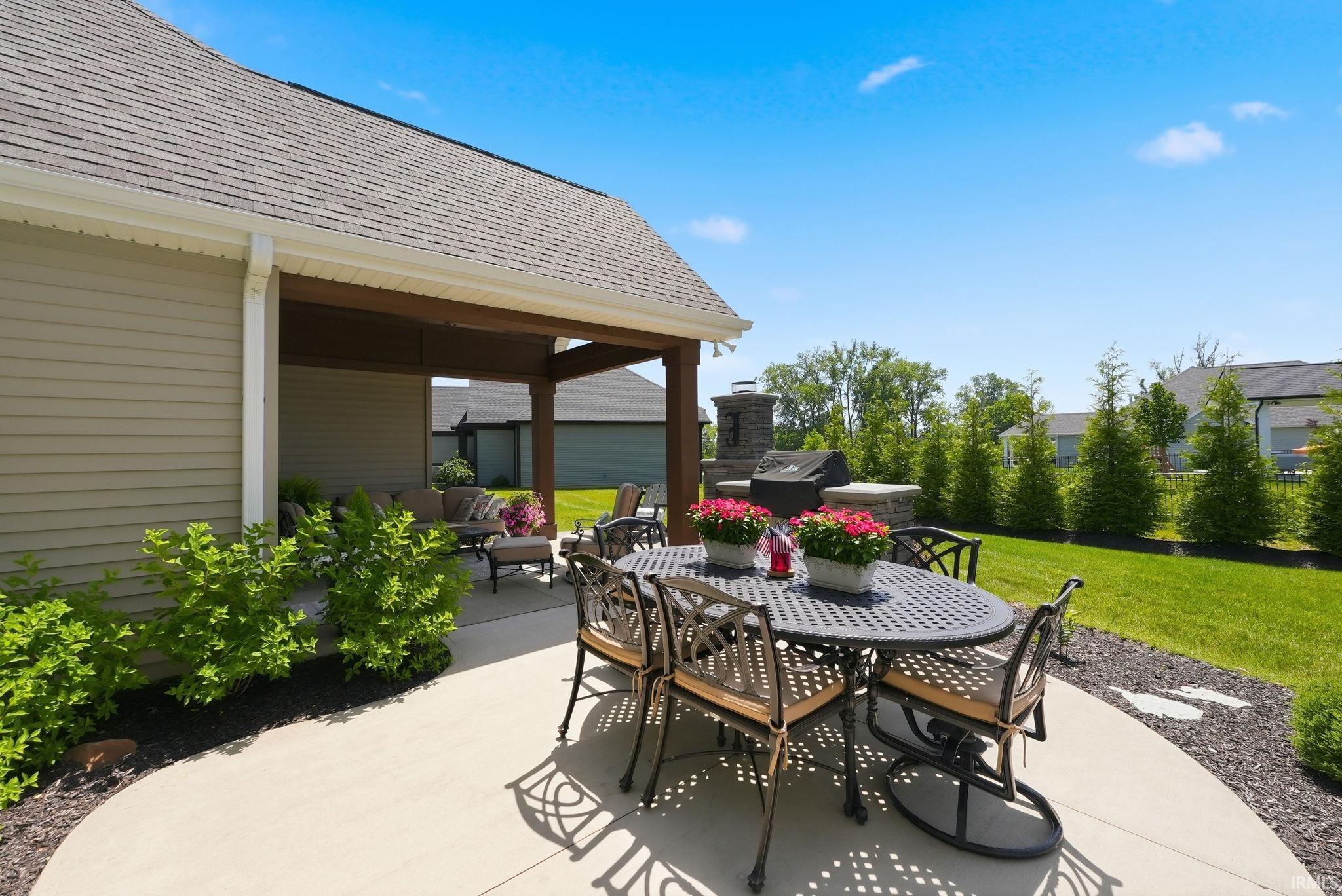 Expansive concrete patio offering a covered outdoor living area and an outdoor kitchen with a stone-clad fireplace