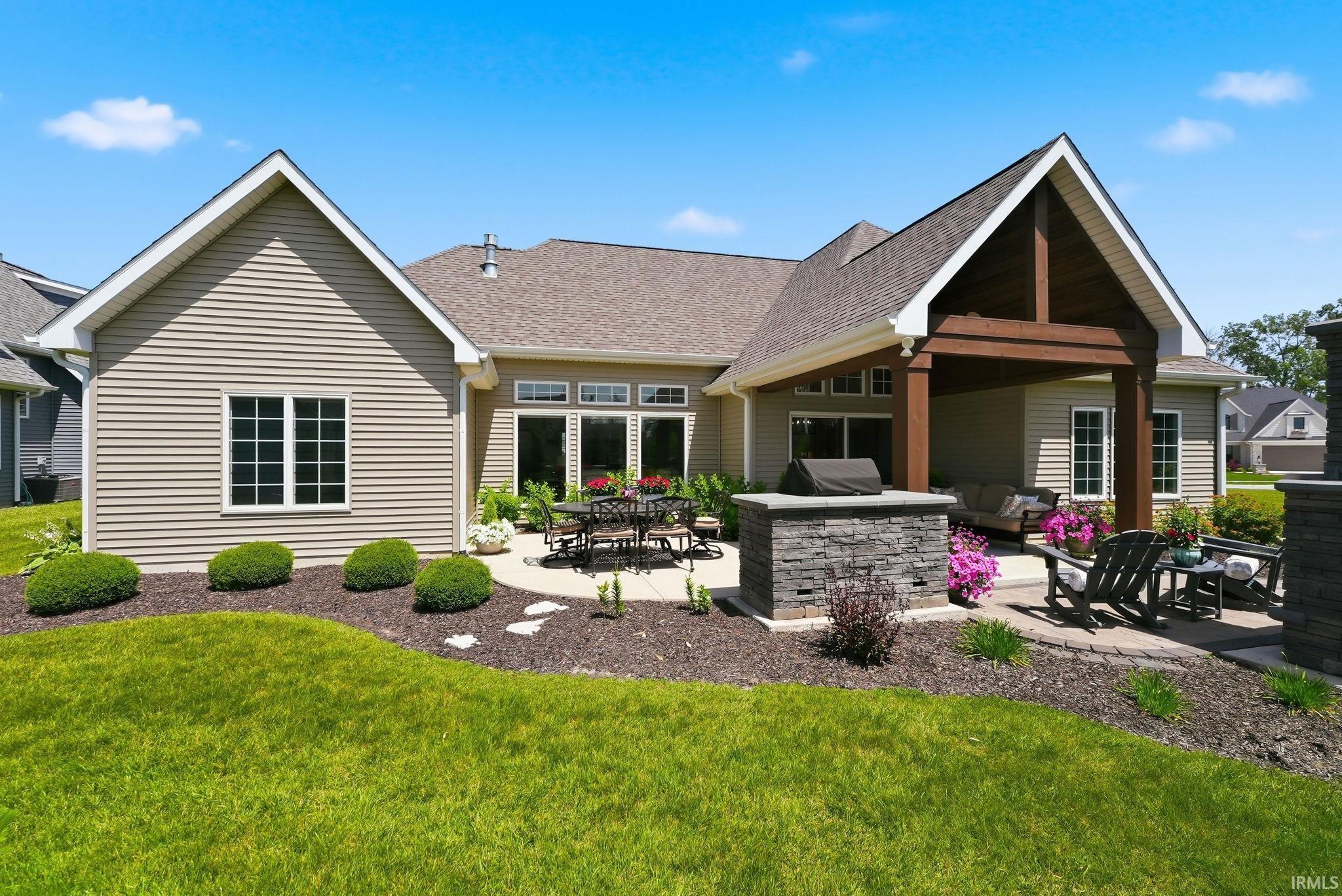 Expansive backyard featuring a manicured lawn, a stone patio, and a covered outdoor living area