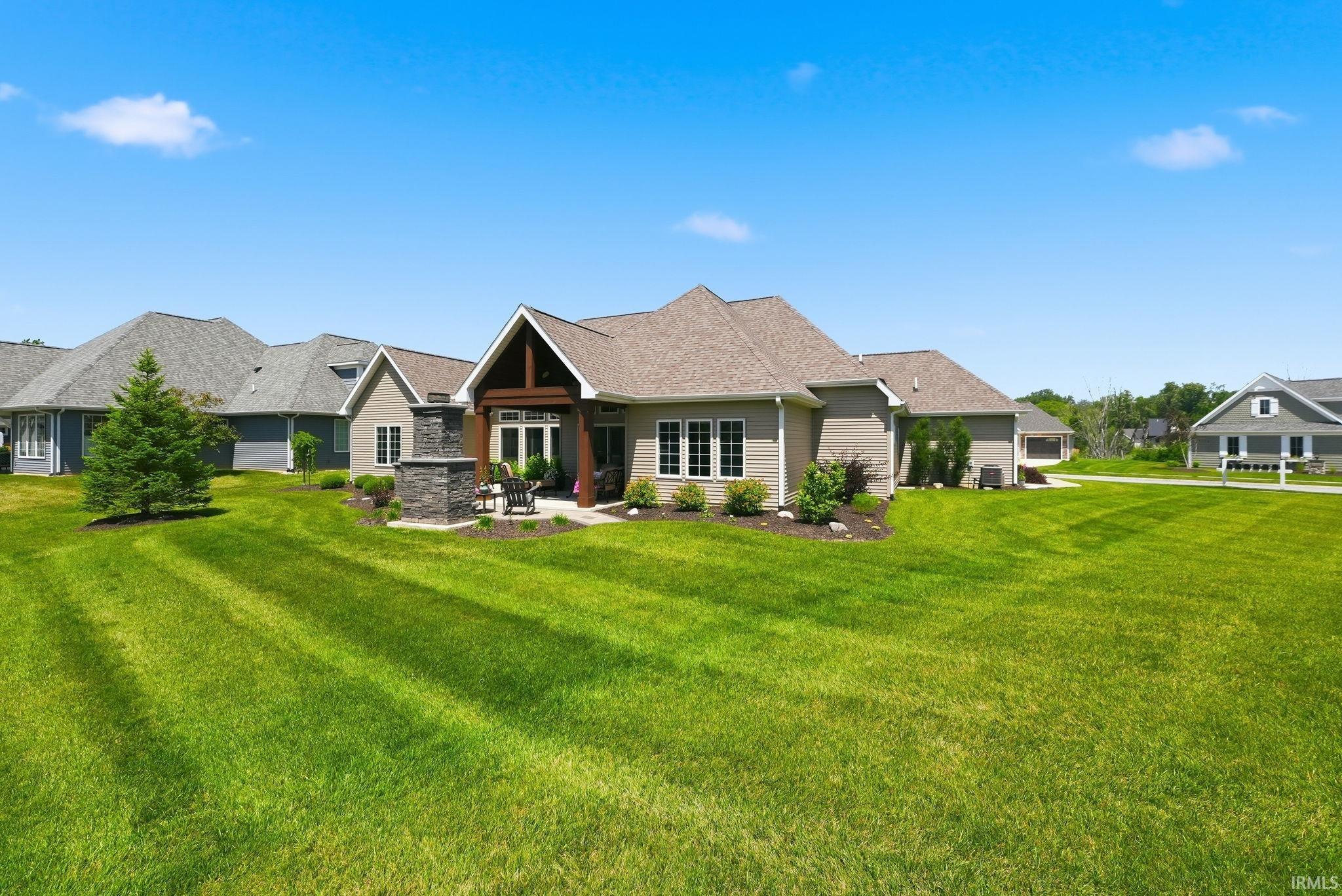 Spacious backyard featuring a stone patio with a built-in outdoor fireplace, covered porch with exposed beams, and multiple windows across the home's rear façade, all surrounded by extensive lawn