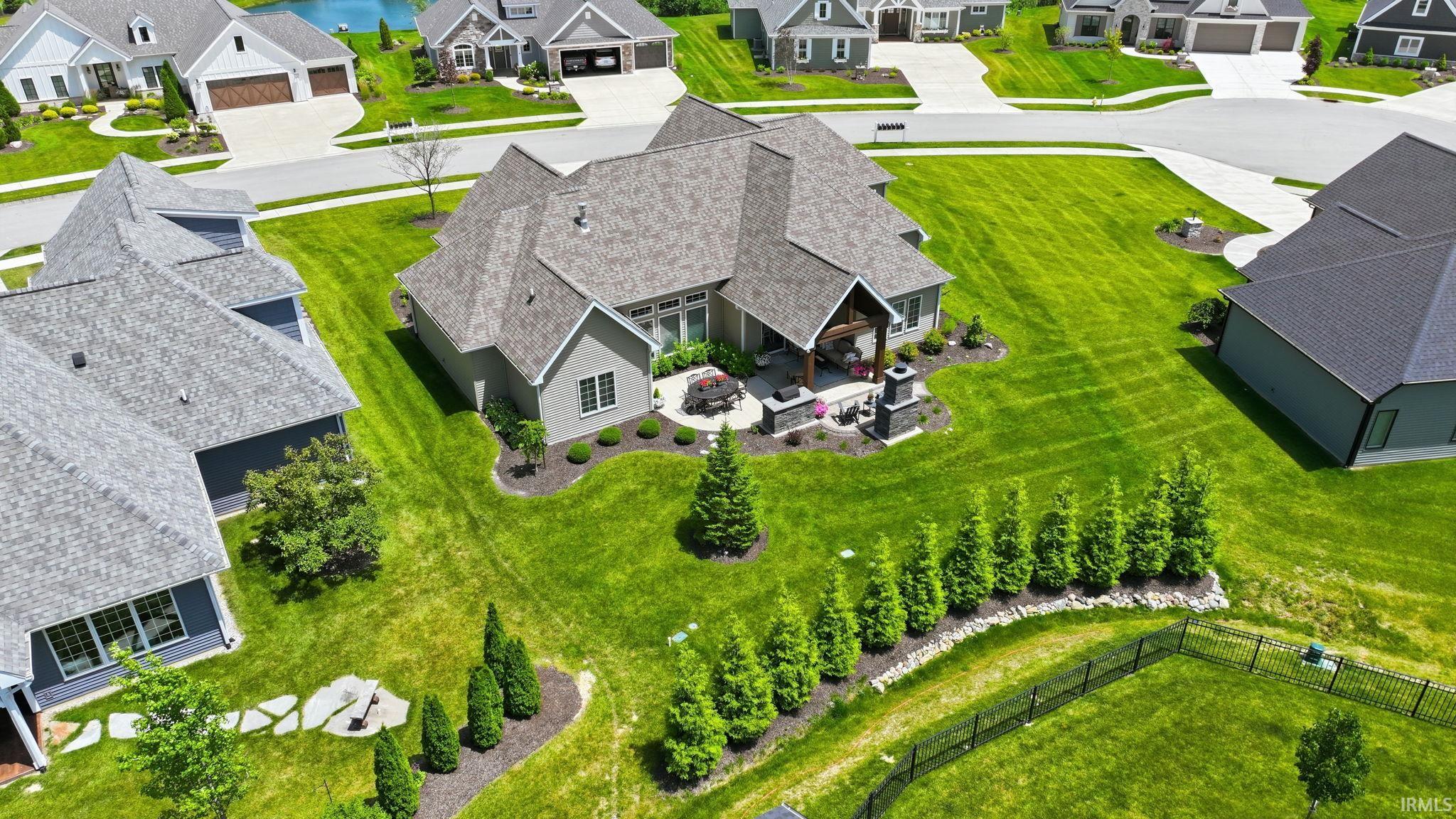 Expansive property featuring a grey-toned exterior, a spacious rear patio with a fireplace, a covered outdoor living area, extensive green lawn, and mature landscaping