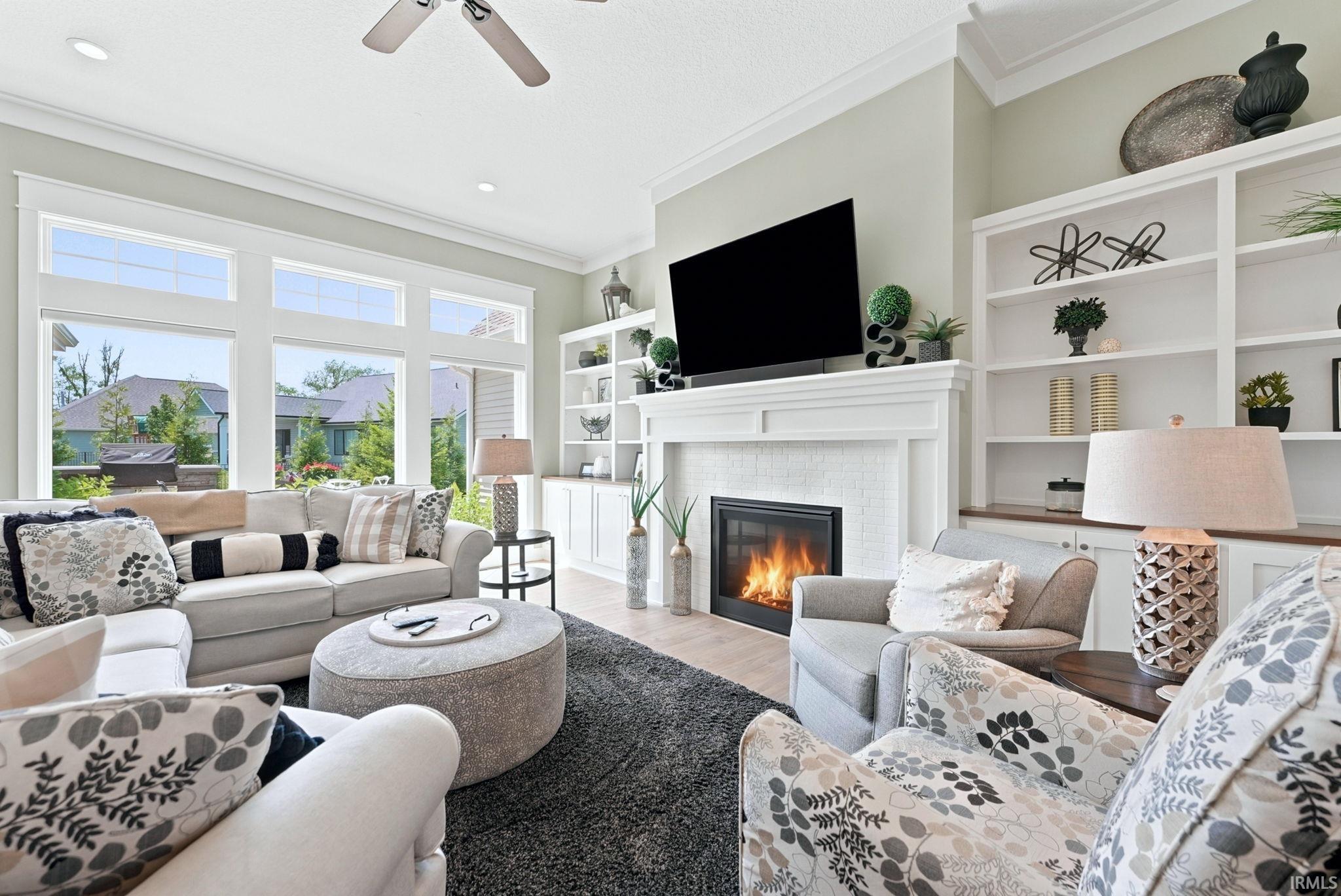 Living area featuring a floor-to-ceiling fireplace with a white mantel, built-in shelving, a ceiling fan, and large windows