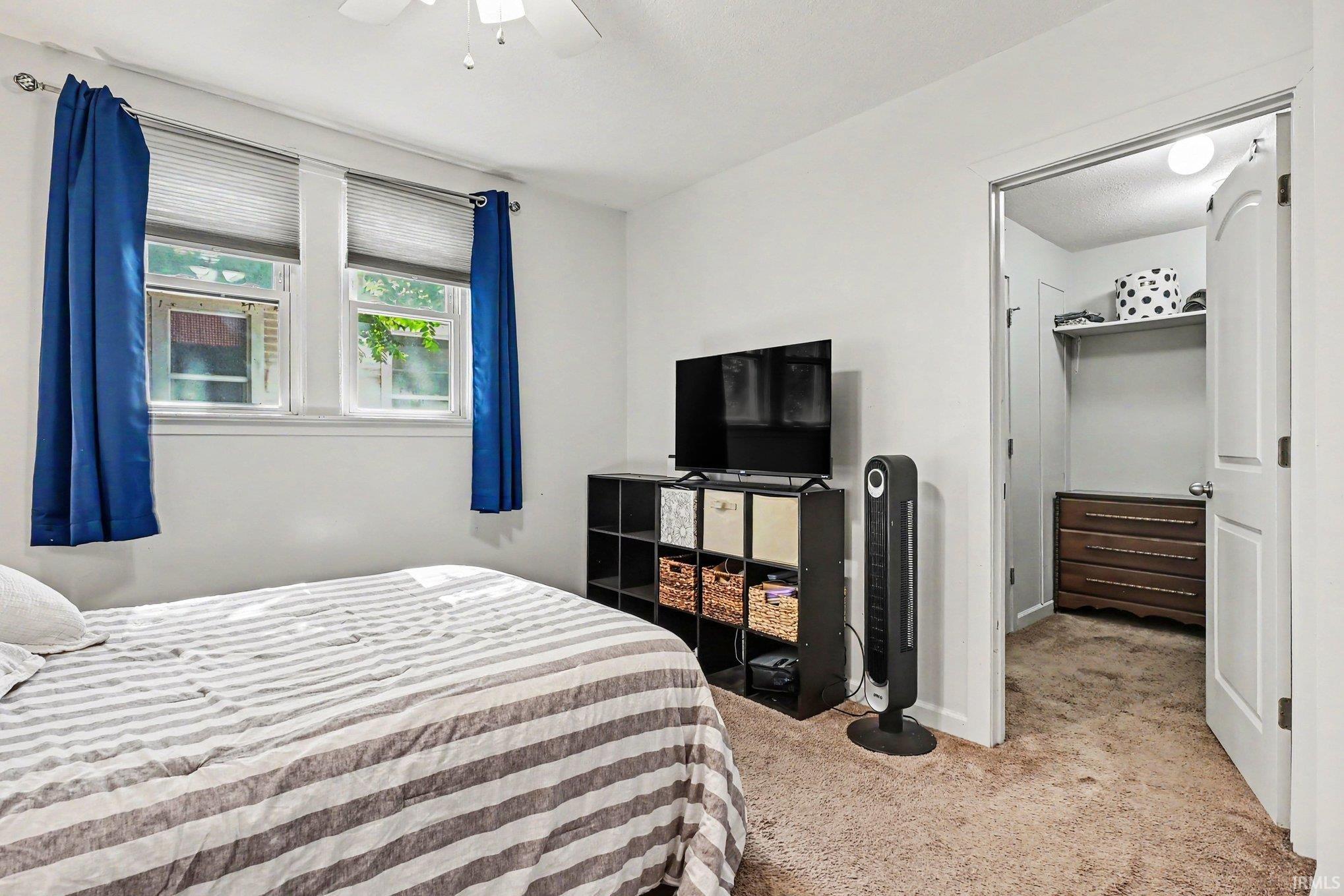 Bright bedroom with two windows featuring privacy blinds, light-colored walls, and neutral carpeting