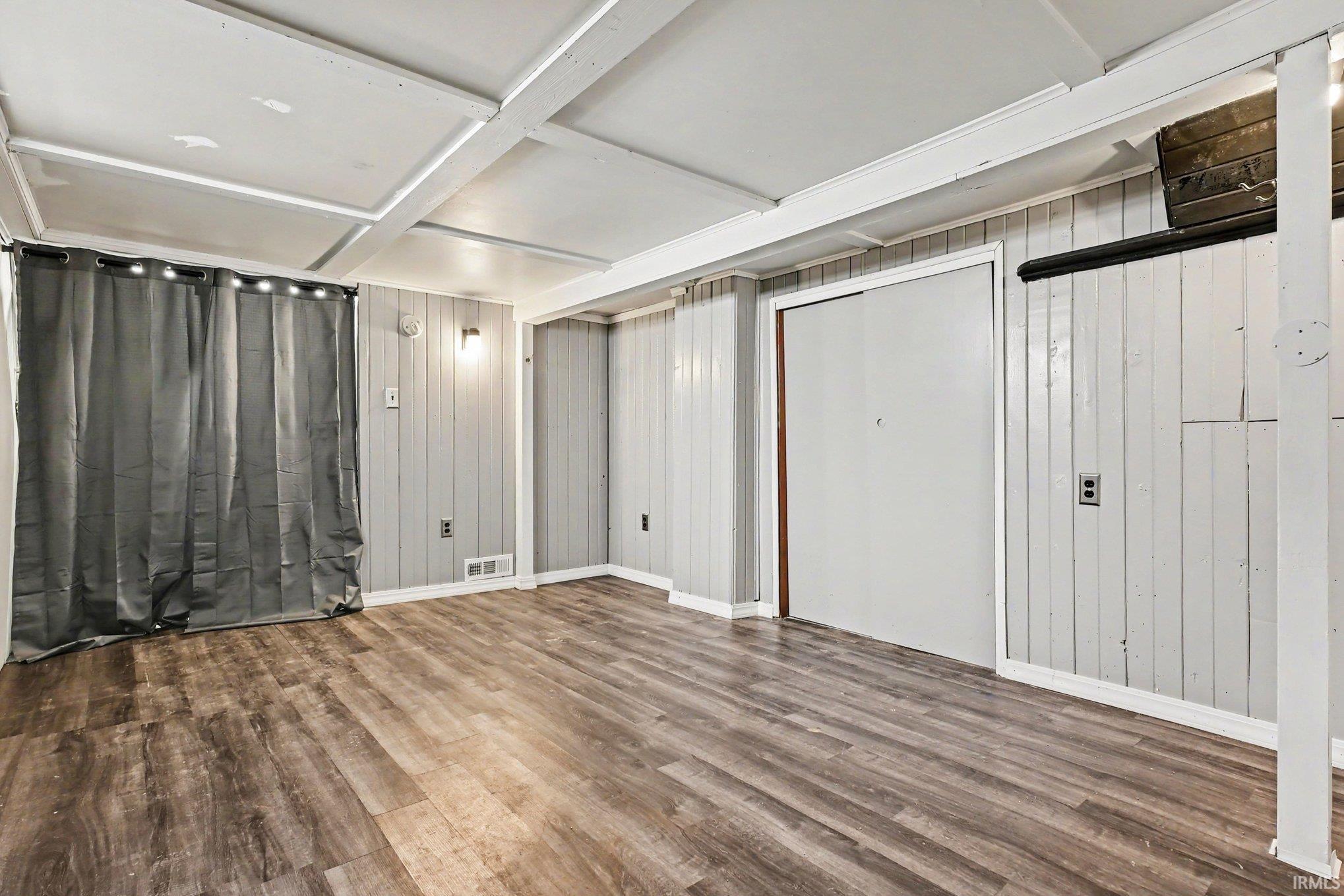 Finished interior space featuring wood-finish flooring, light grey vertical paneling, and a white coffered ceiling