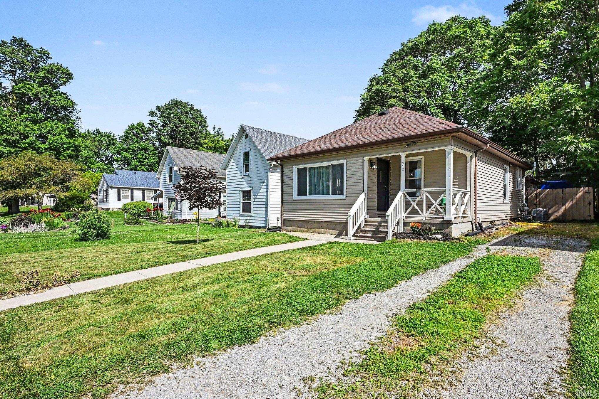 Single-story residence featuring light-colored horizontal siding, a covered front porch with white railings, and a gravel driveway