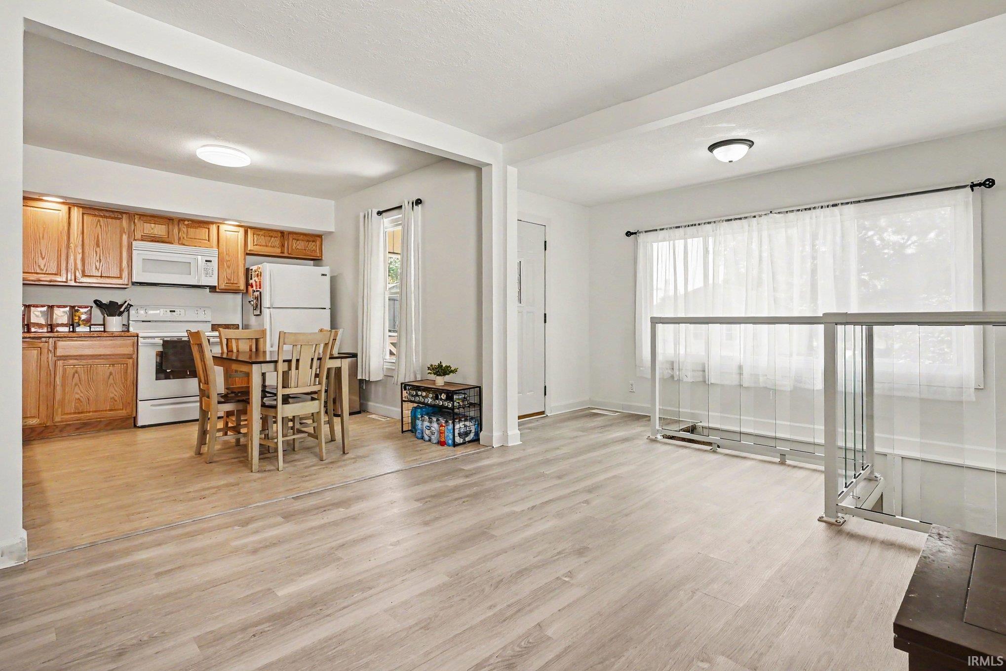 Bright interior featuring light wood-finish flooring, white walls, and a kitchen with wood cabinetry and white appliances
