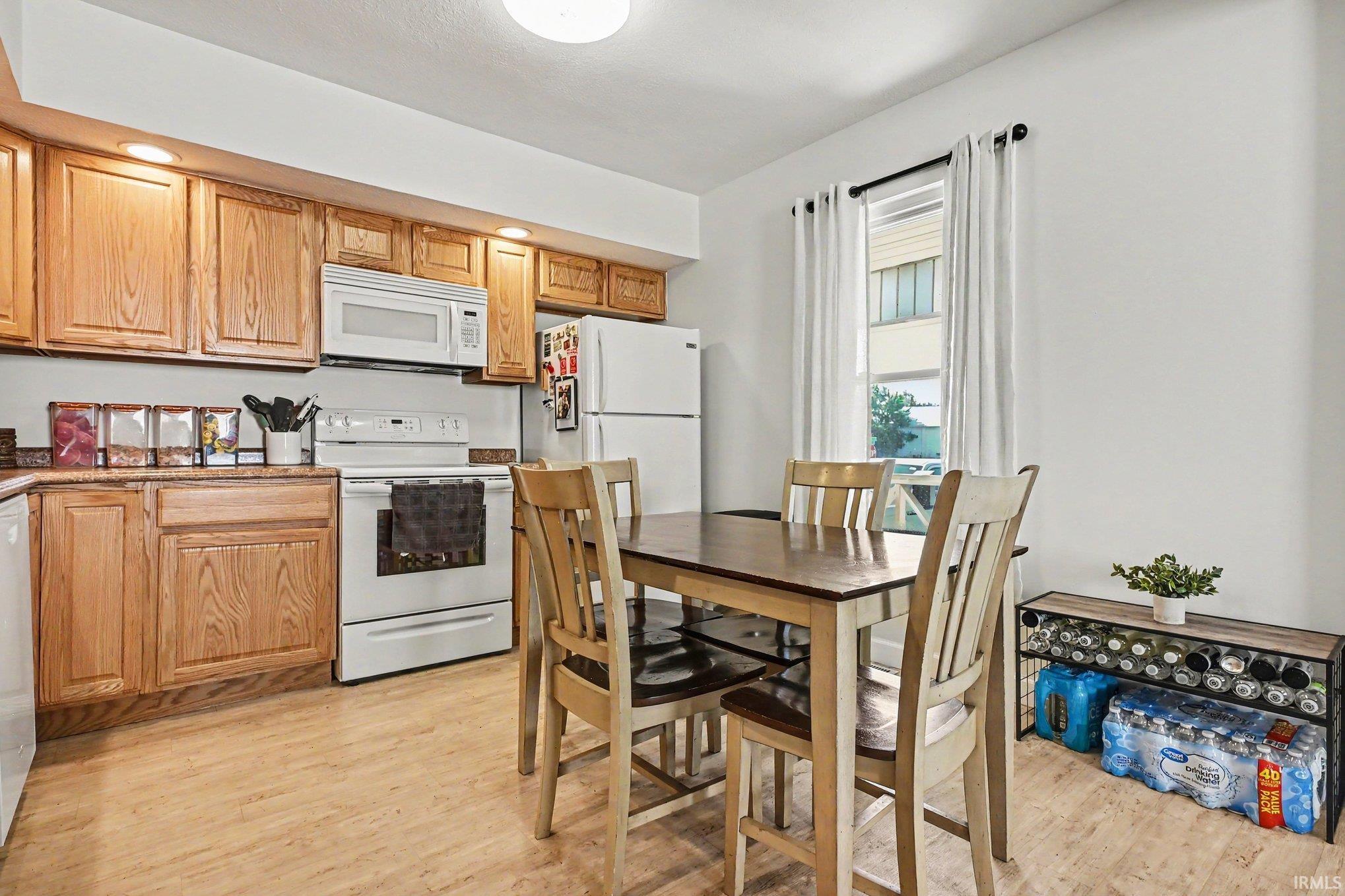 Kitchen featuring wood cabinetry, white appliances, laminate countertops, and wood-finish flooring