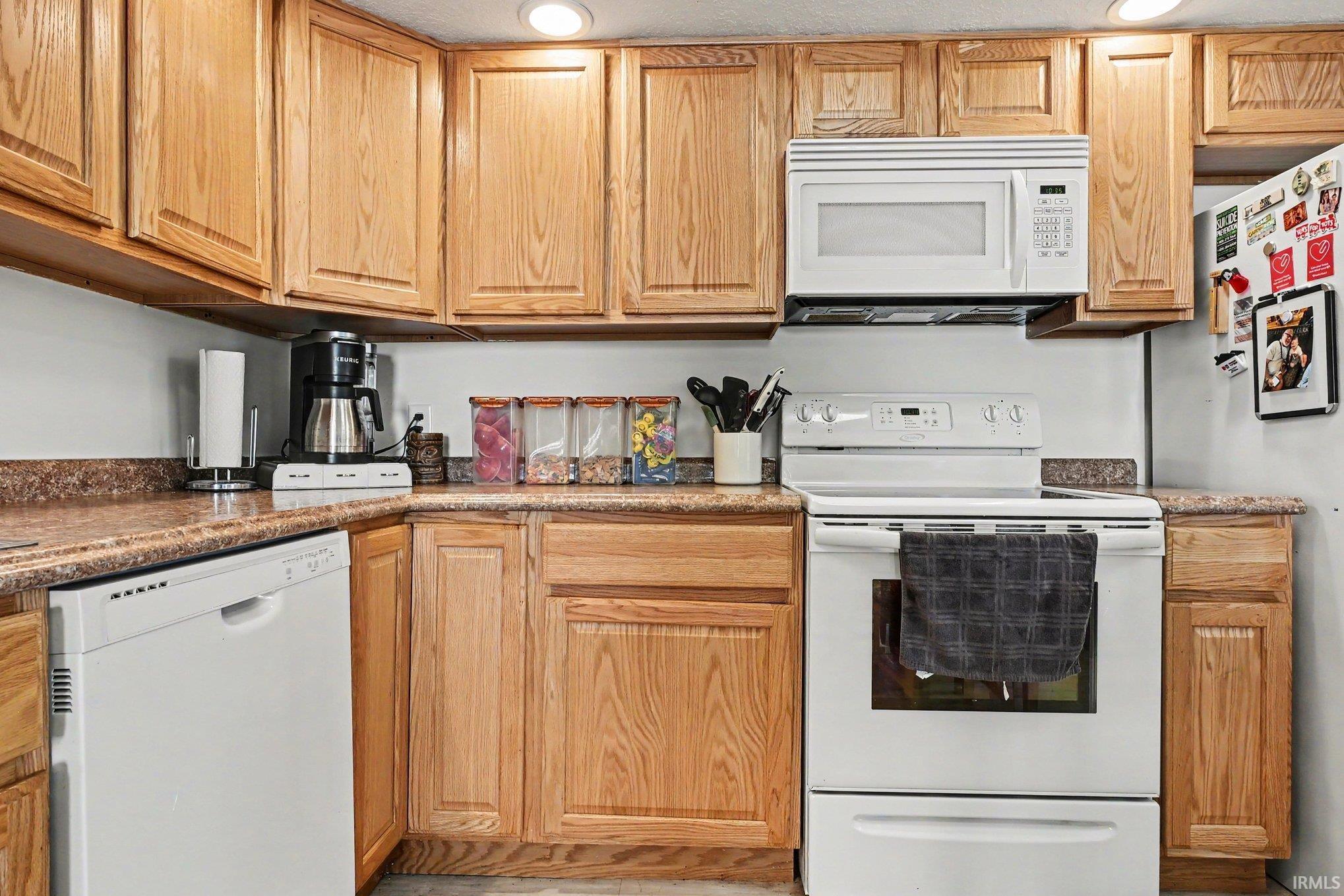 Kitchen featuring wood cabinetry, white appliances, and speckled countertops