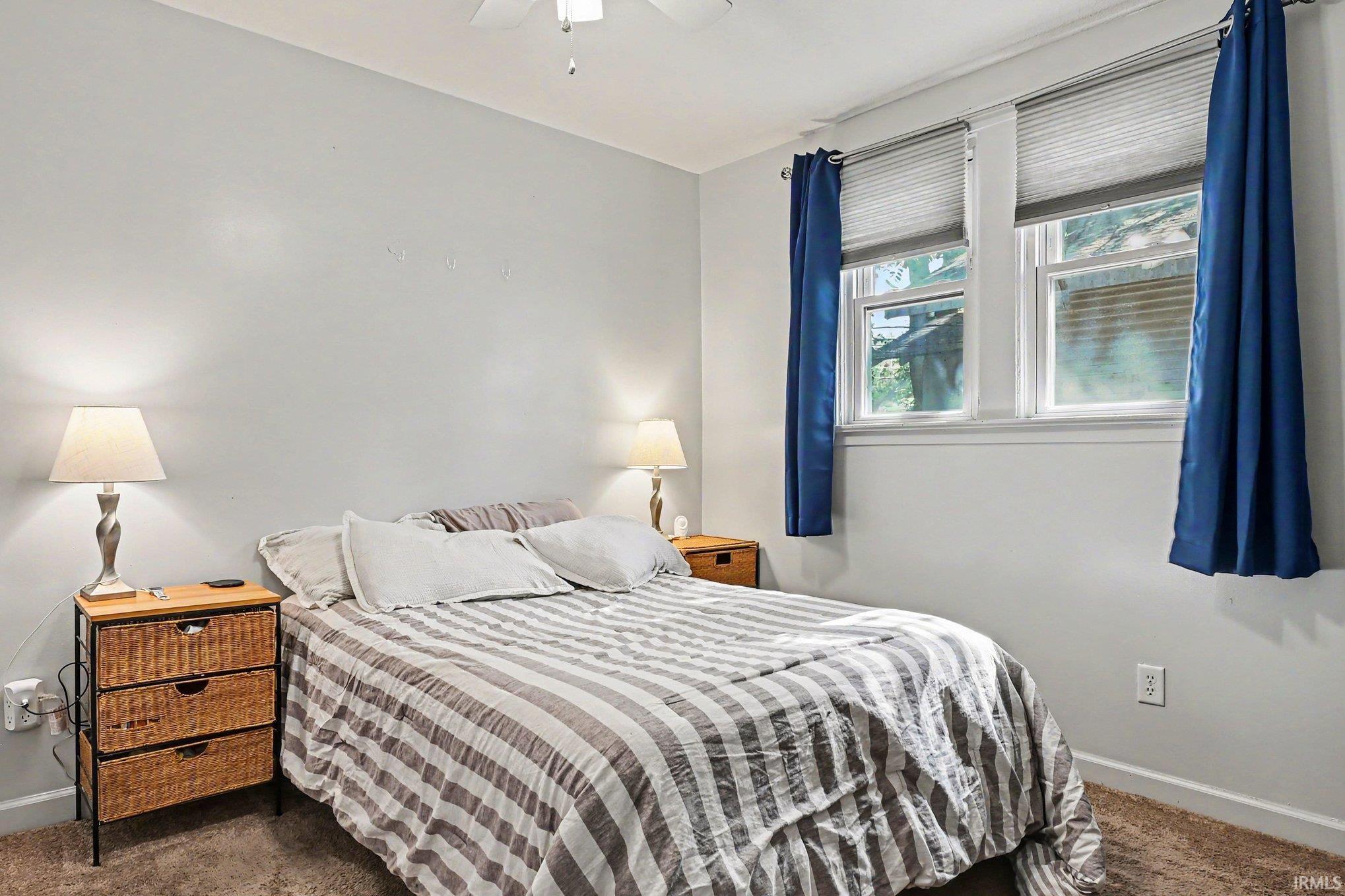 Light gray walls with white trim, two double-hung windows with white frames, carpeted flooring, and a ceiling fan