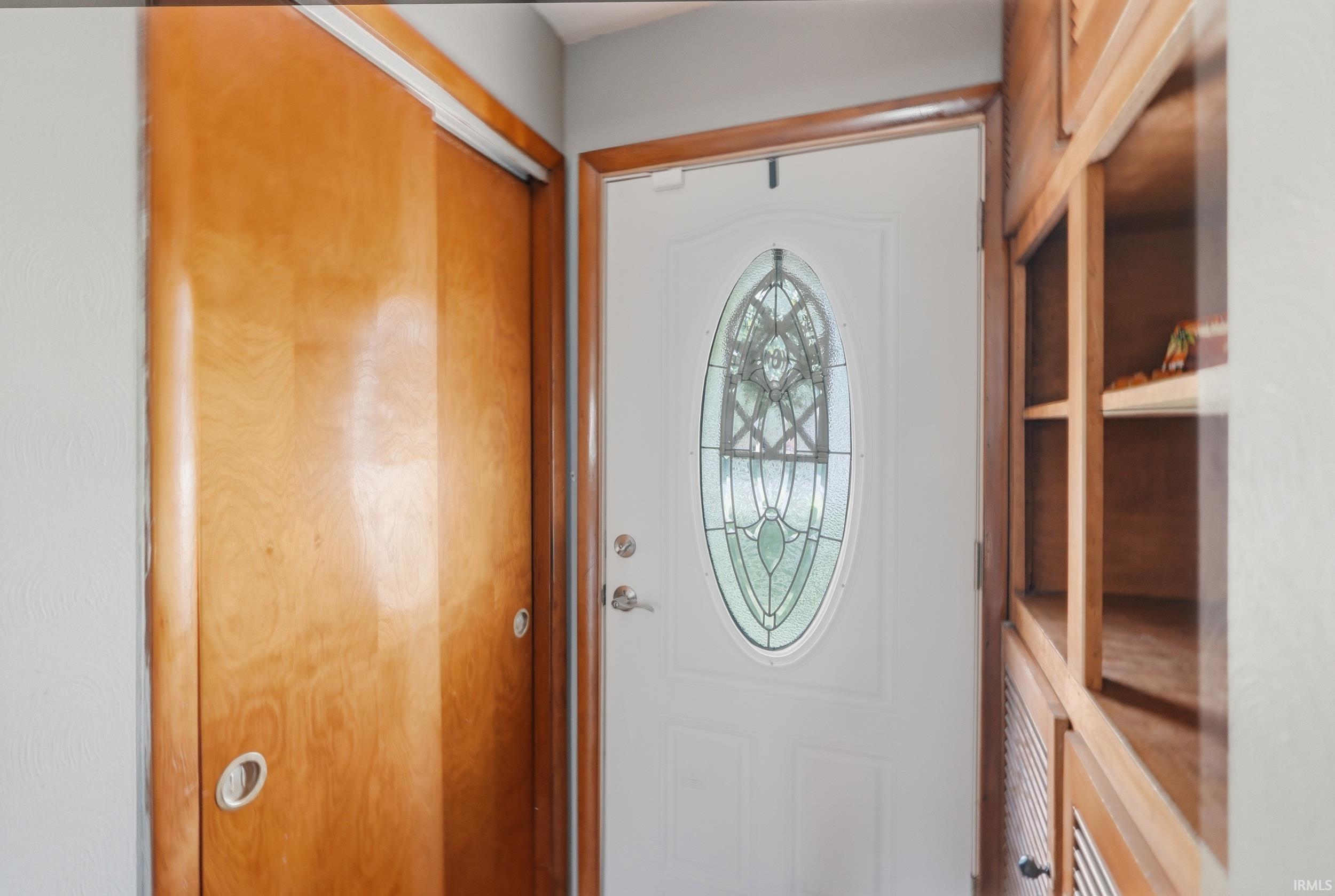 Entryway featuring a white door with an oval stained glass insert, wood-finish sliding closet doors, and built-in wood-finish shelving and cabinetry