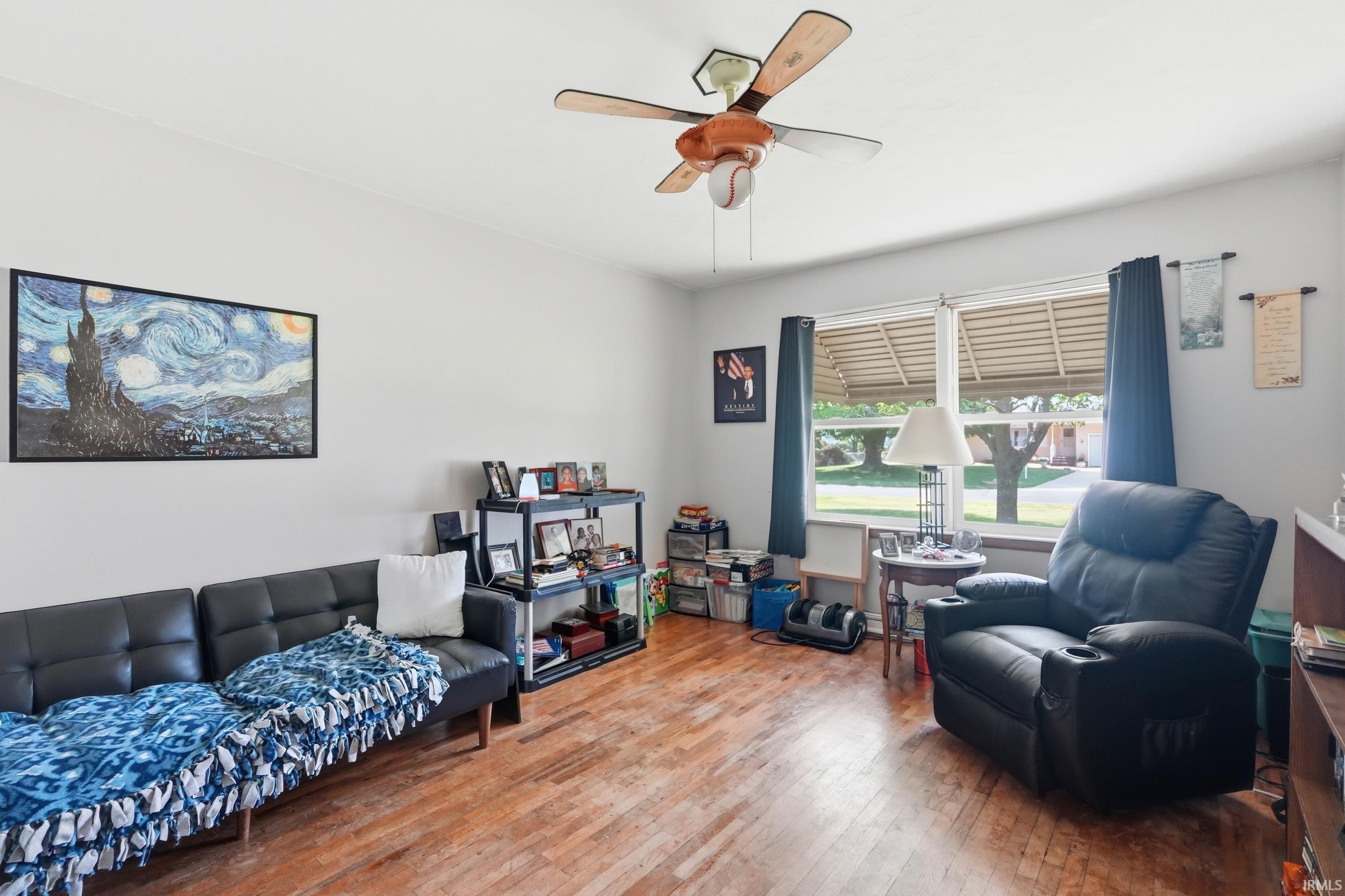 Bright living area featuring wood-finish flooring, a ceiling fan with integrated lighting, and multiple windows providing natural light