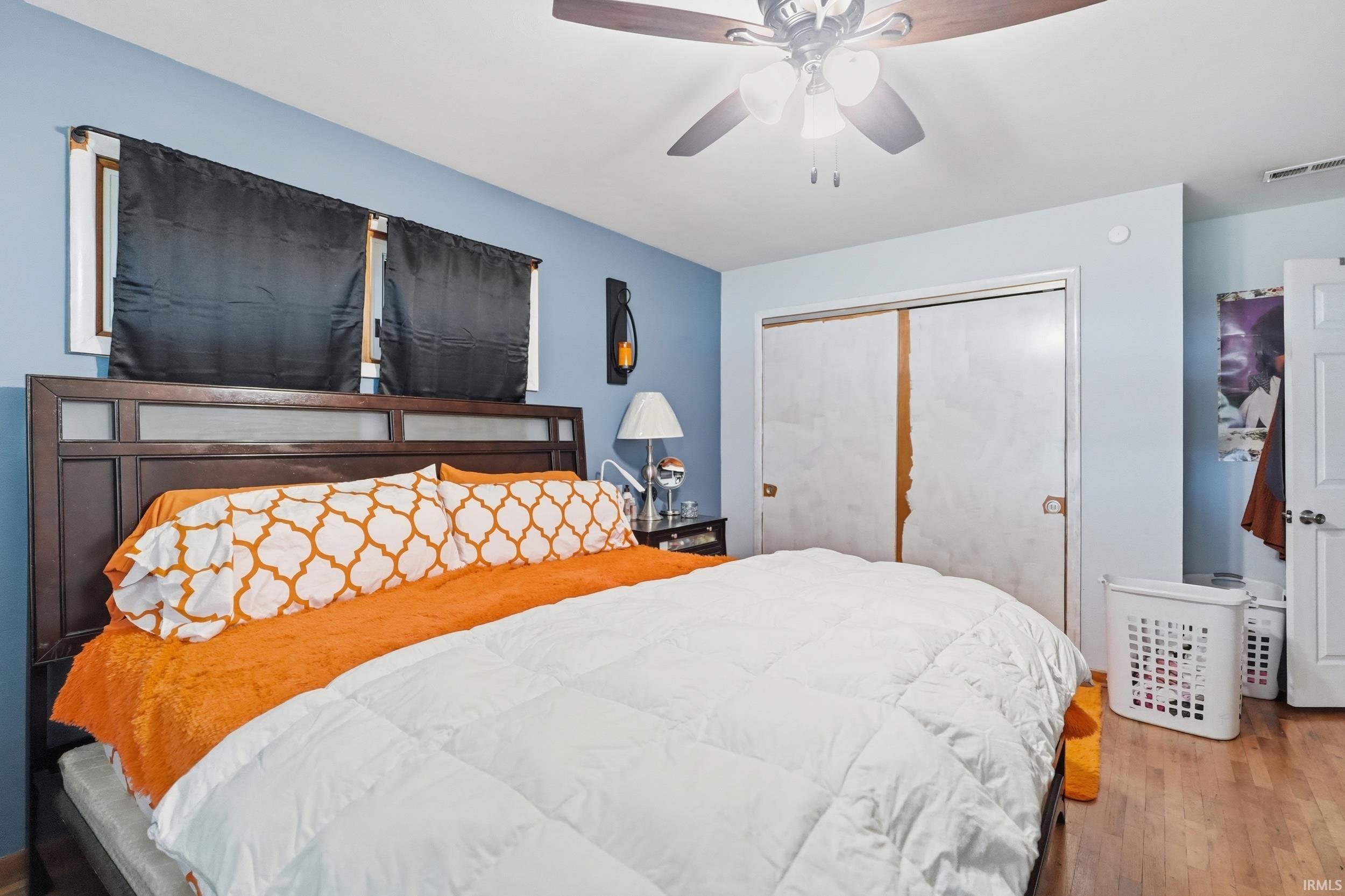 Bedroom featuring wood-finish flooring, two windows, a ceiling fan, and sliding closet doors