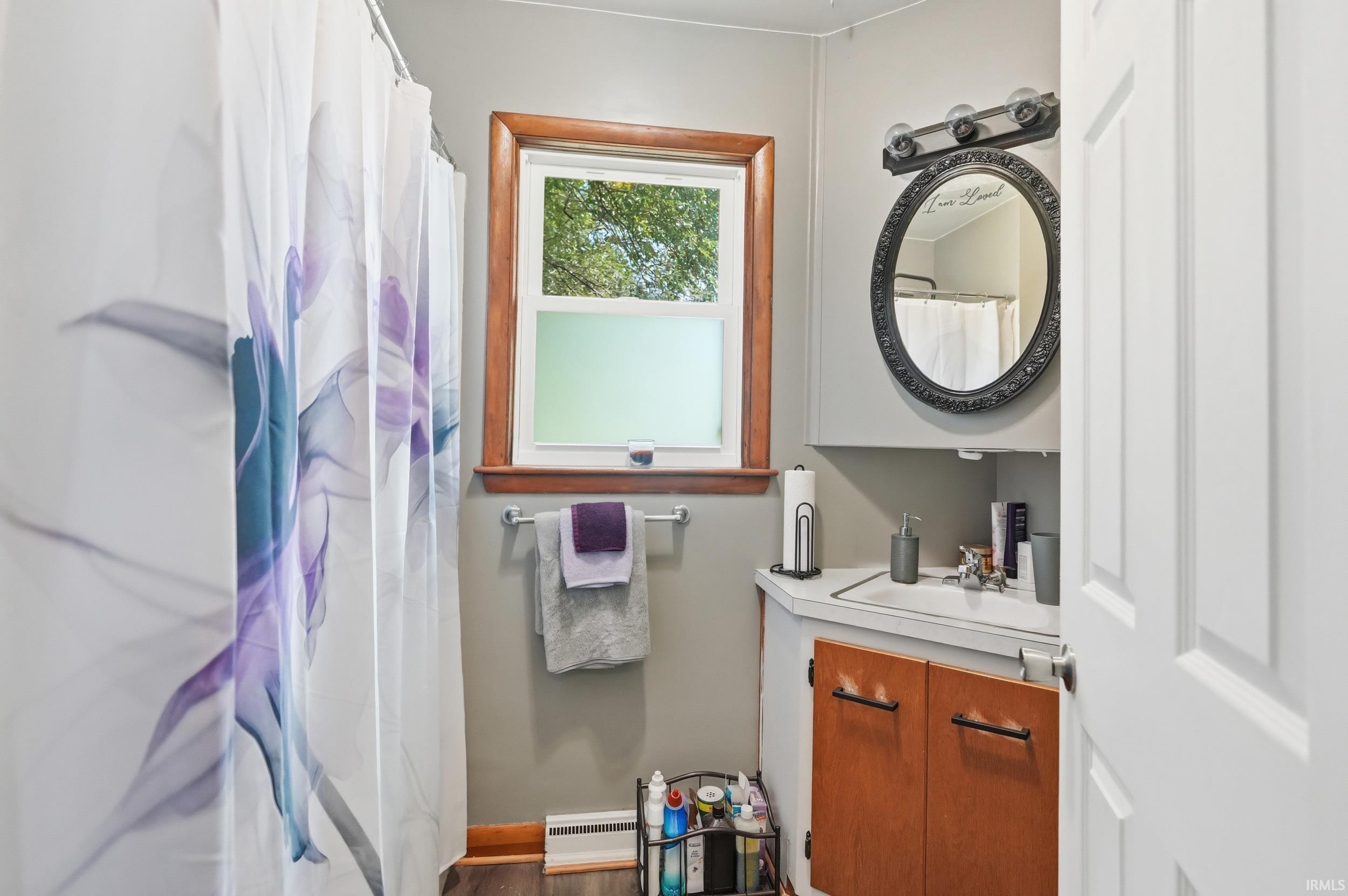 Bathroom with a window featuring wood trim, a corner vanity with integrated sink, and an ornate framed mirror with overhead lighting
