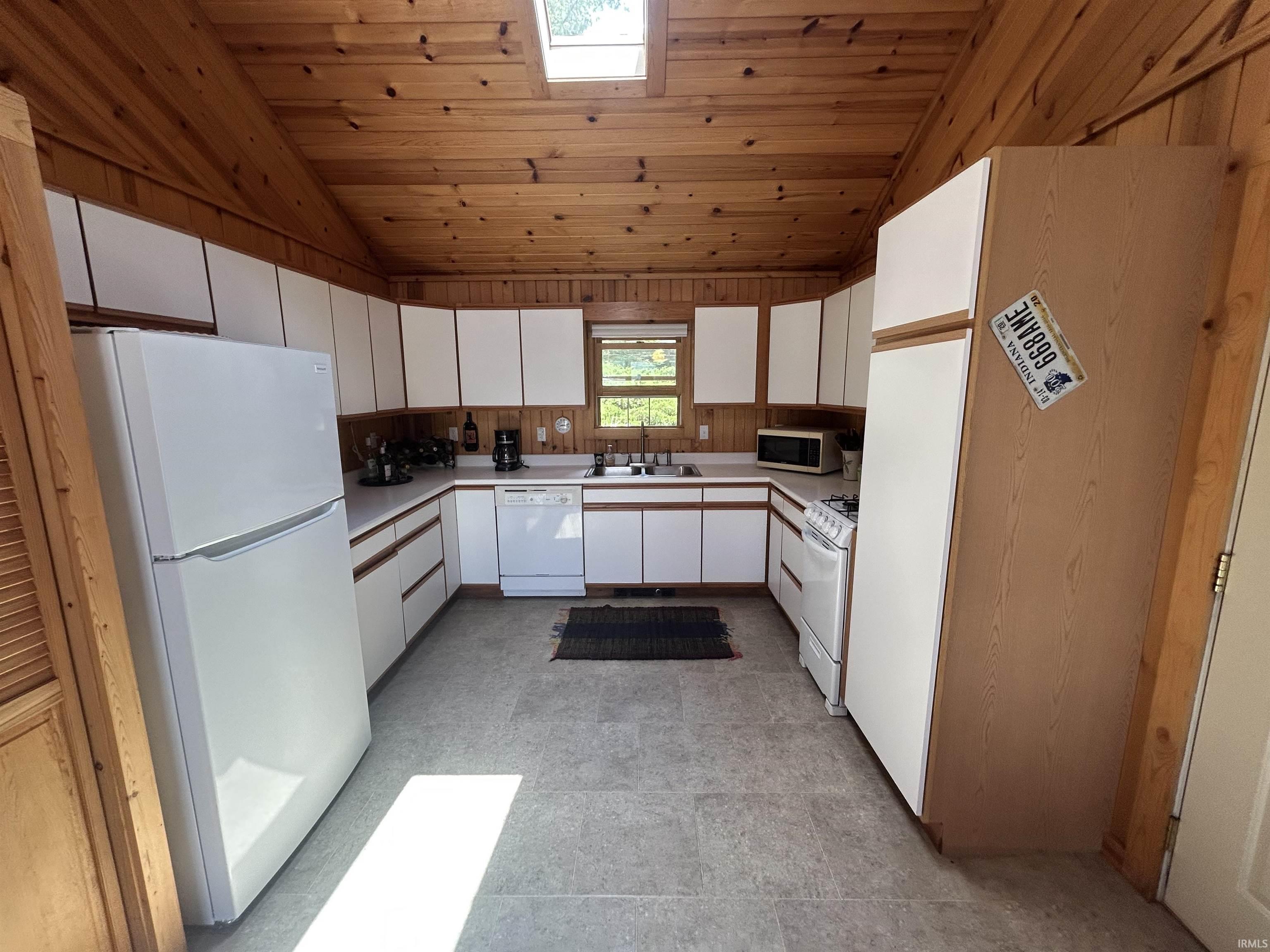 Kitchen featuring extensive wood paneling, white cabinetry, a skylight, and light grey flooring
