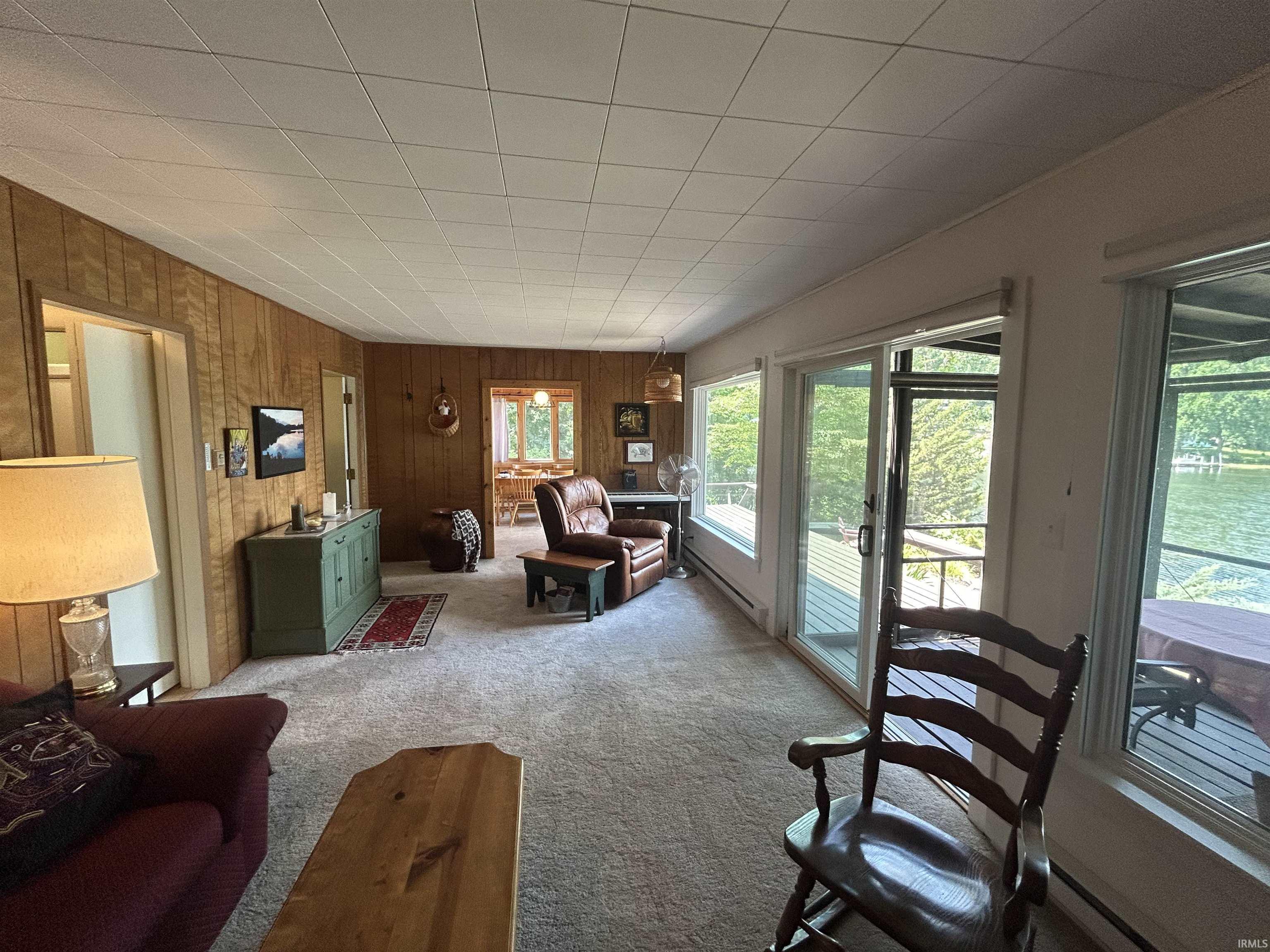 Living area featuring wood paneling, carpet flooring, a drop ceiling, and multiple large windows overlooking water