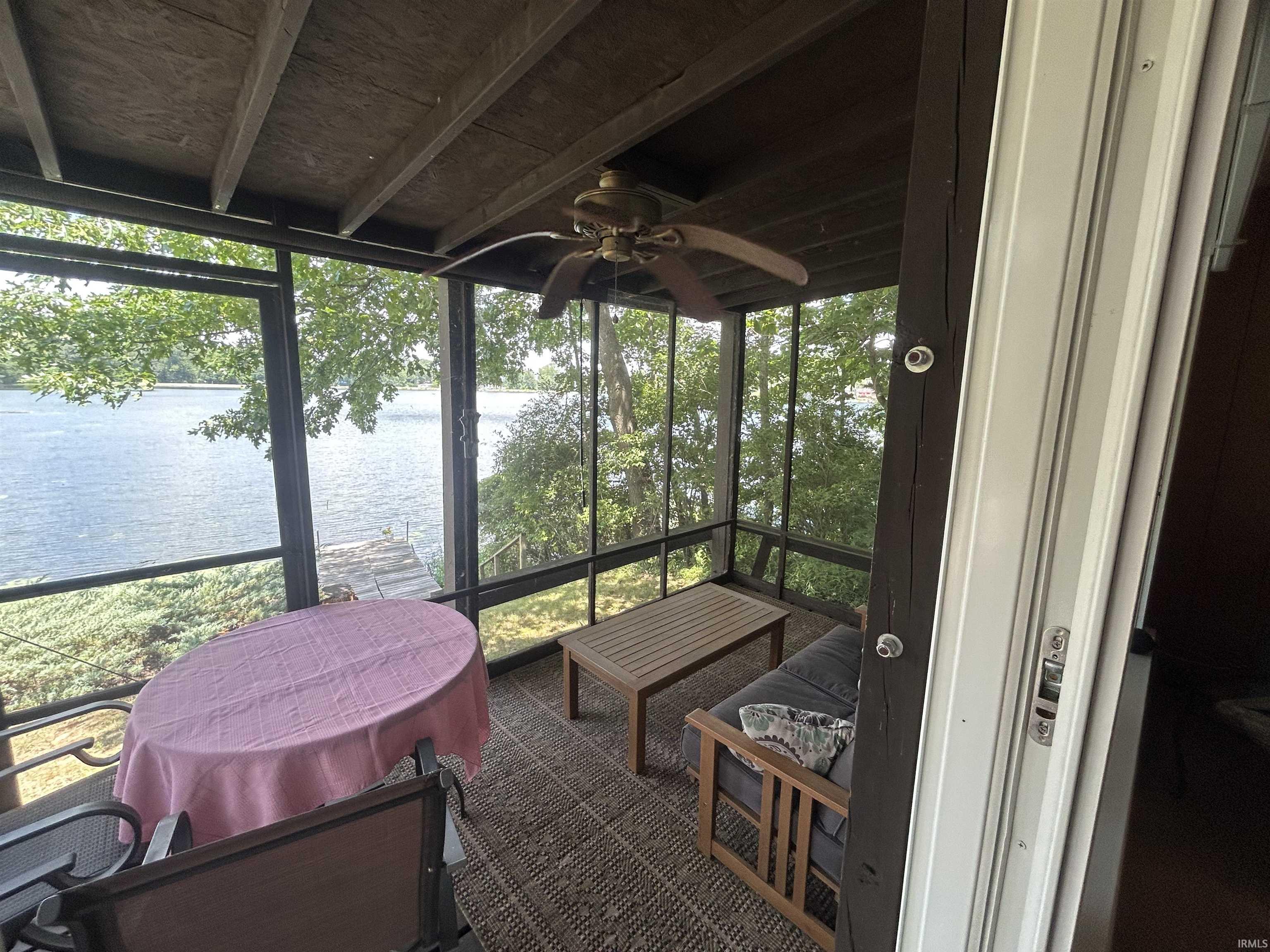 Screened porch with water scenery, exposed wood beam ceiling, ceiling fan, and sliding glass door access