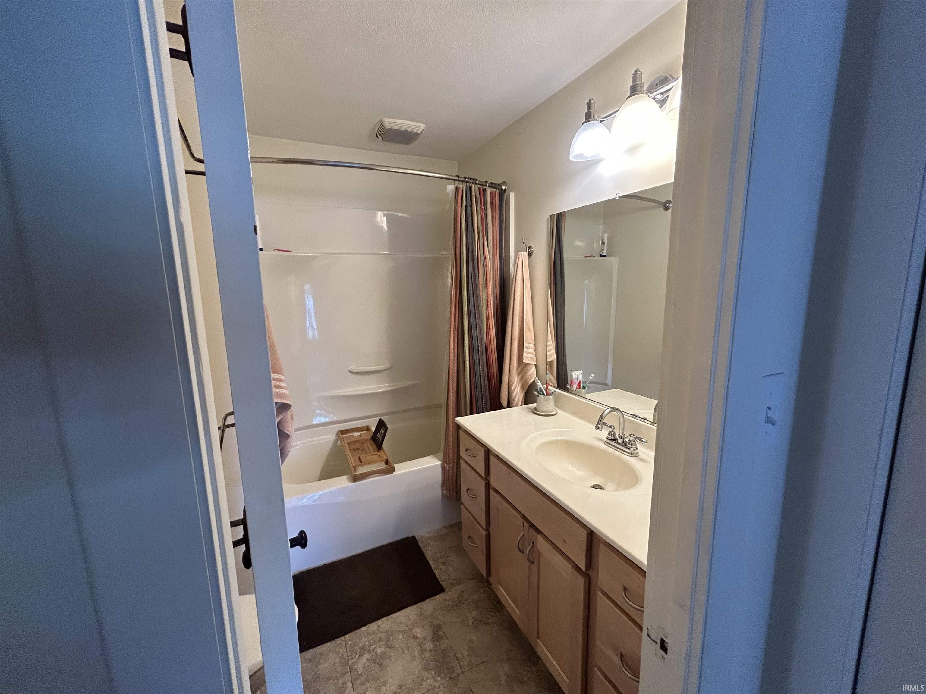 Full bathroom featuring a single vanity with a laminate countertop, chrome faucet, and wood-finish cabinetry