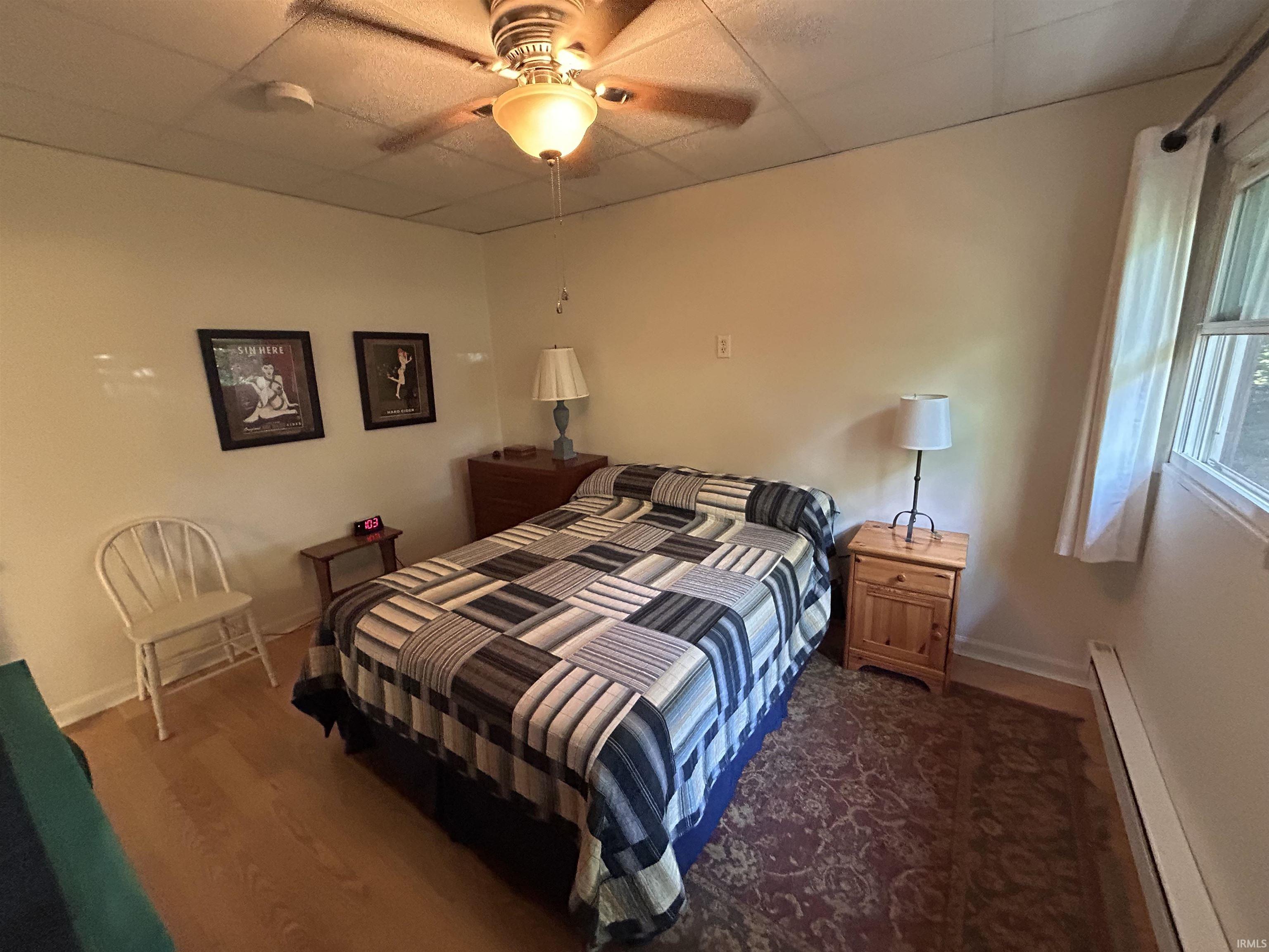 Bedroom featuring a ceiling fan with integrated lighting, wood-finish flooring, a window providing natural light, and perimeter baseboard heating