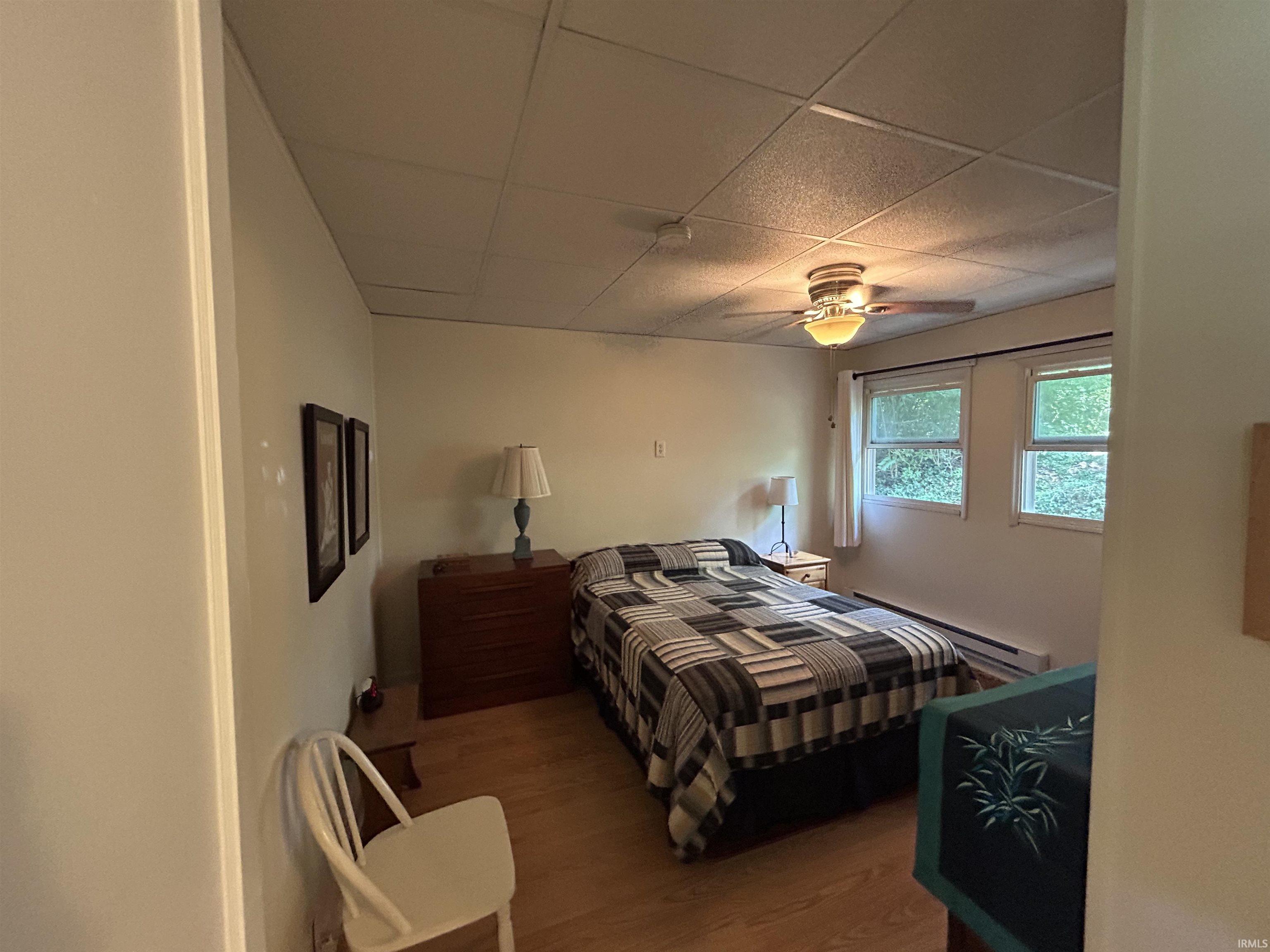 Room featuring light wood-finish flooring, a ceiling fan with integrated lighting, two windows, and light-colored walls