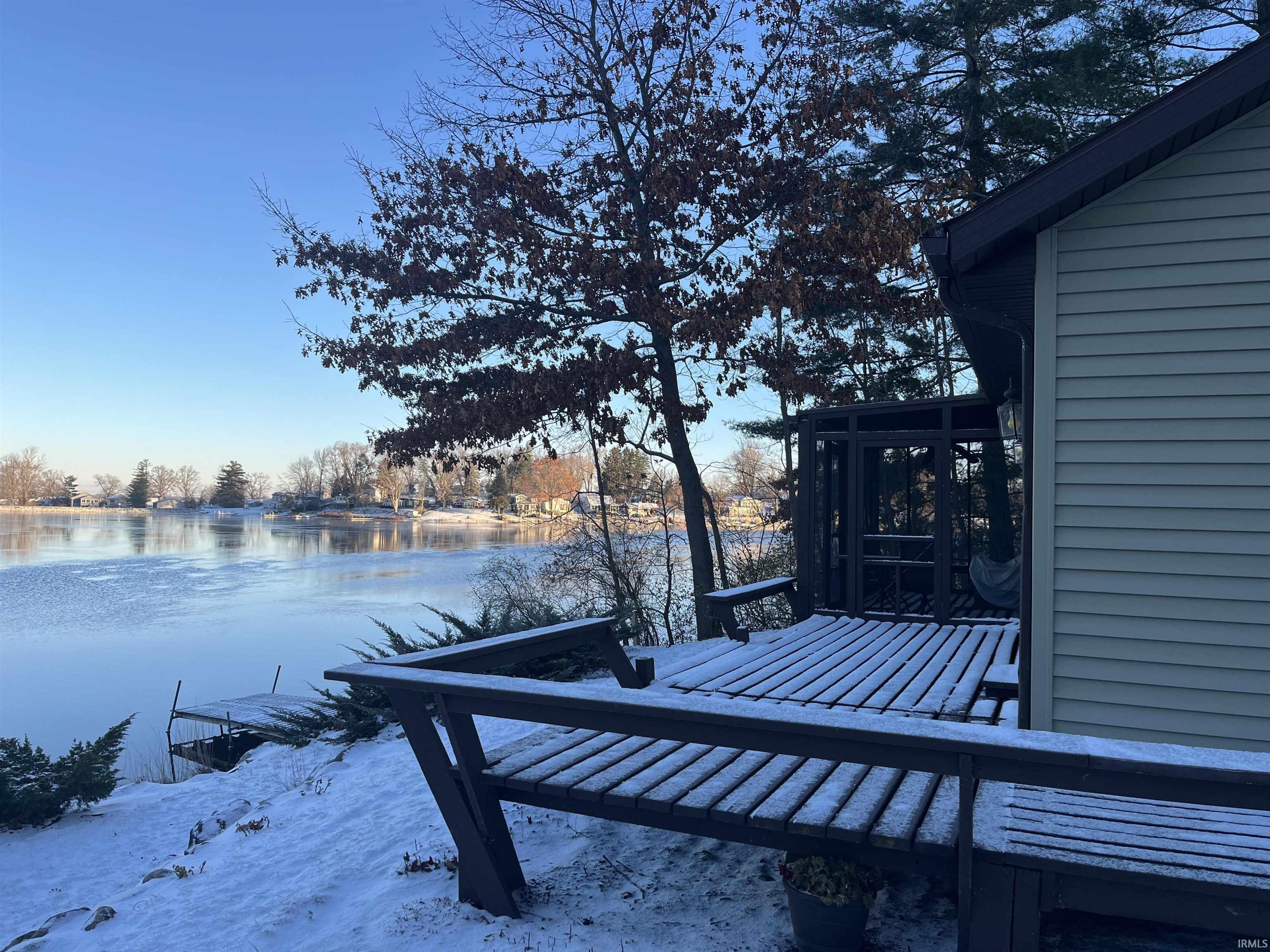 Waterside property featuring a spacious deck with built-in bench seating, a screened-in porch, and a private dock structure