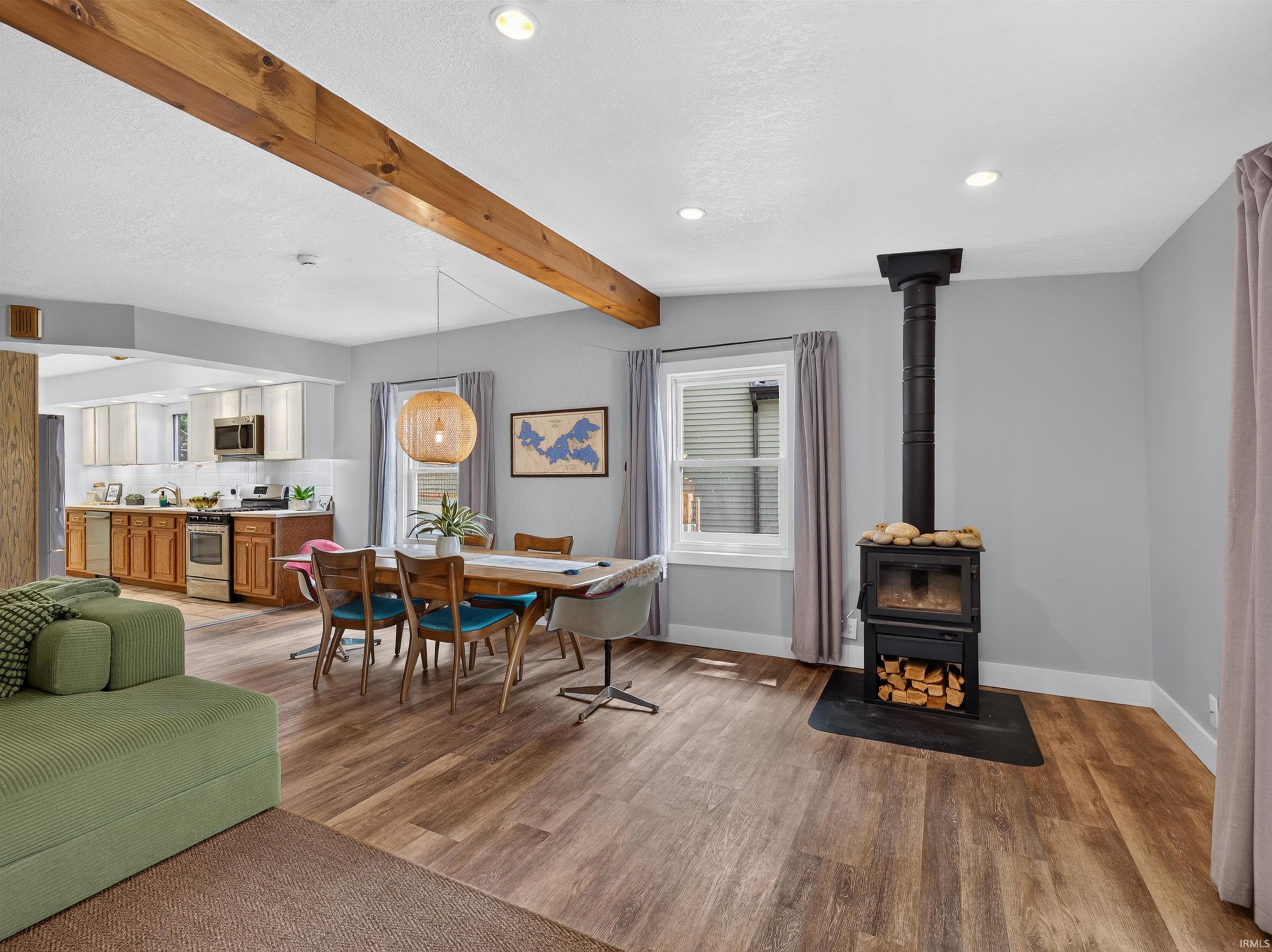 Living area featuring a freestanding wood-burning stove, wood-finish flooring, and an exposed ceiling beam