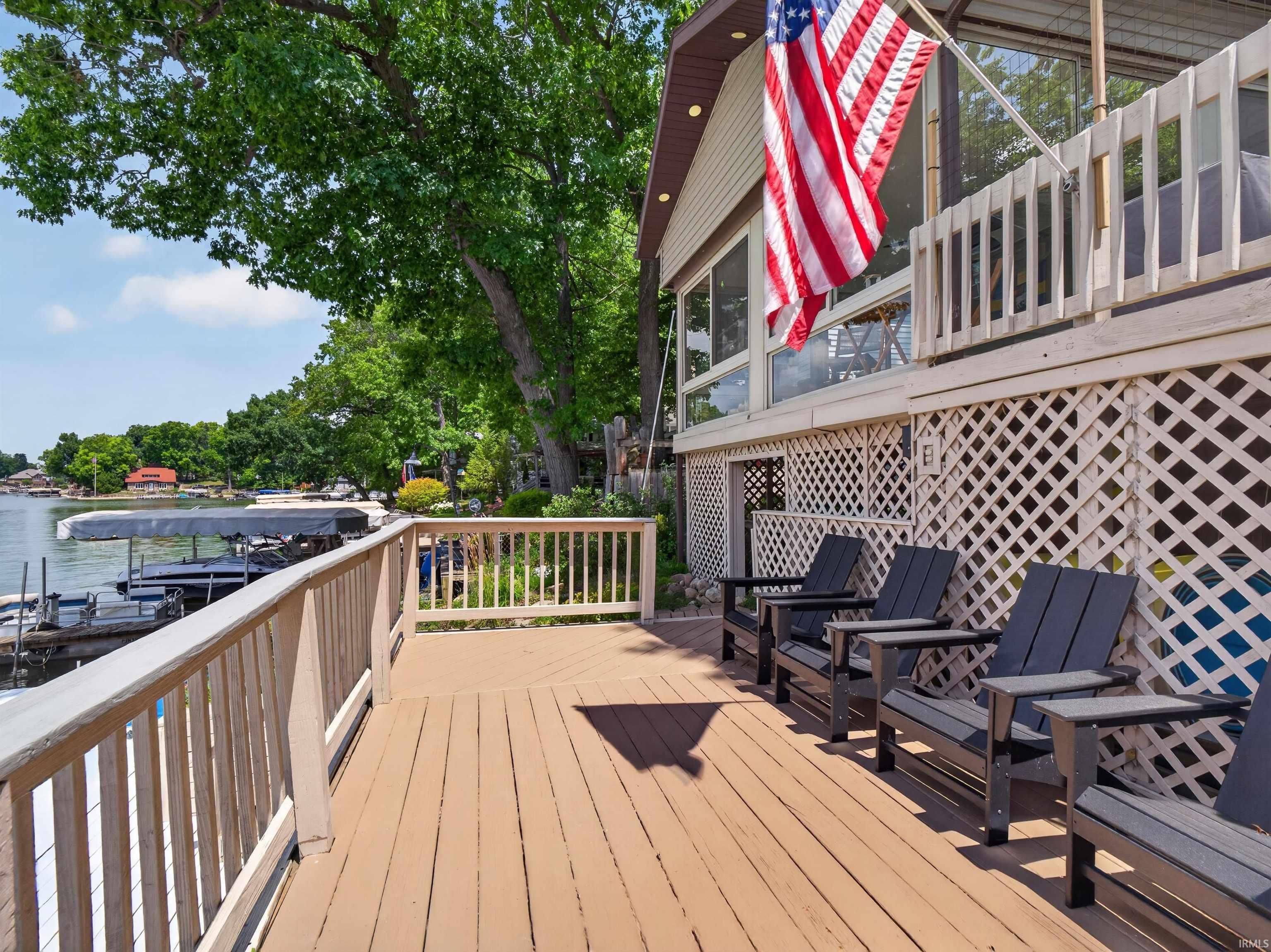Expansive waterfront deck featuring a light brown wood finish, white railings, and direct access to a private dock
