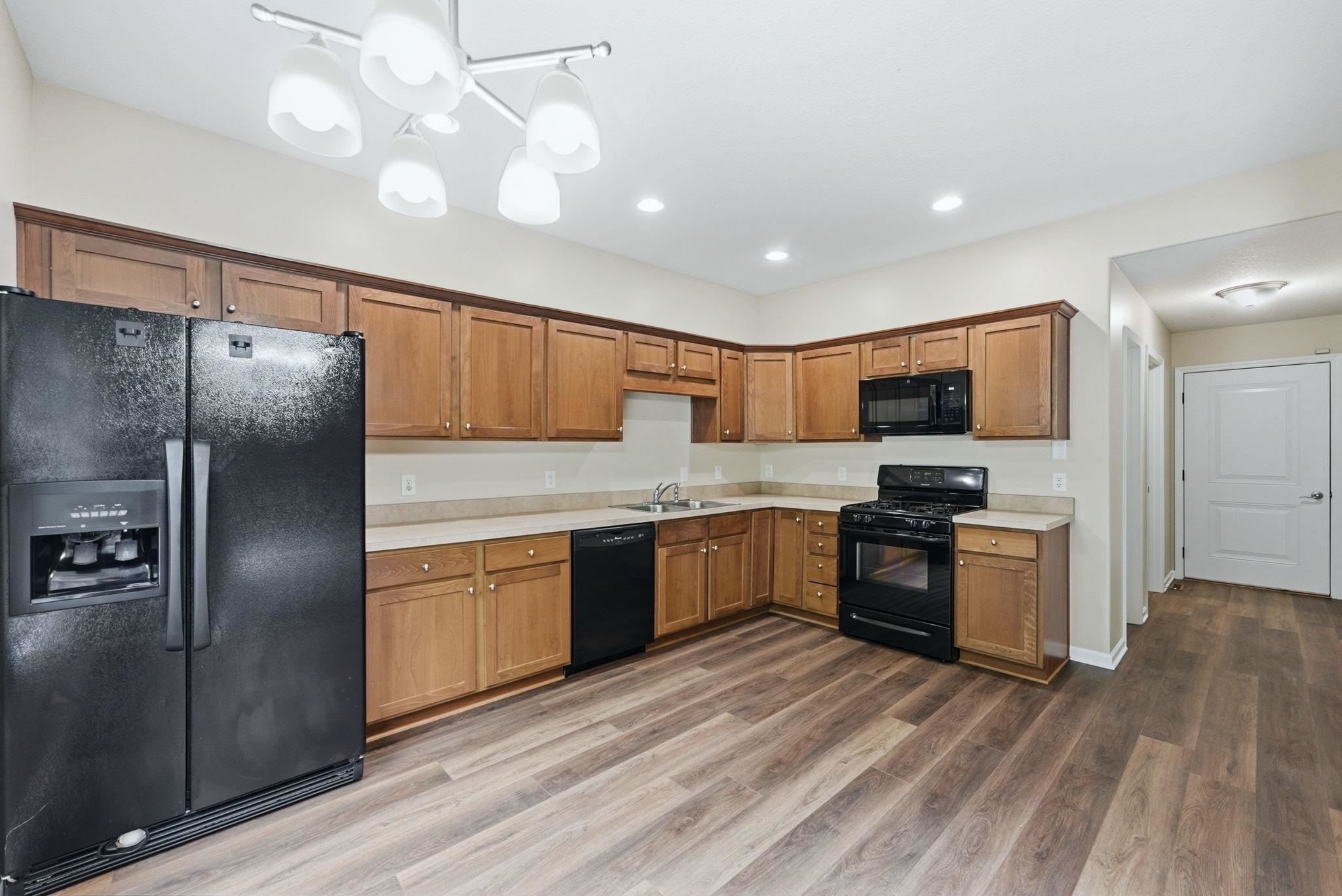 Kitchen featuring wood-finish flooring, a full suite of black appliances, and ample cabinetry