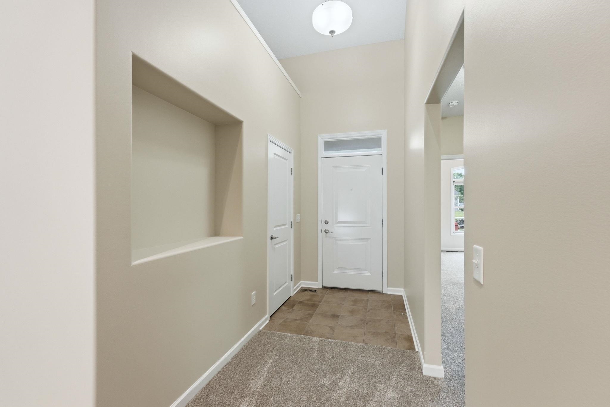 Entryway featuring a white front door with transom window, recessed wall niche, vaulted ceiling, and flush mount lighting