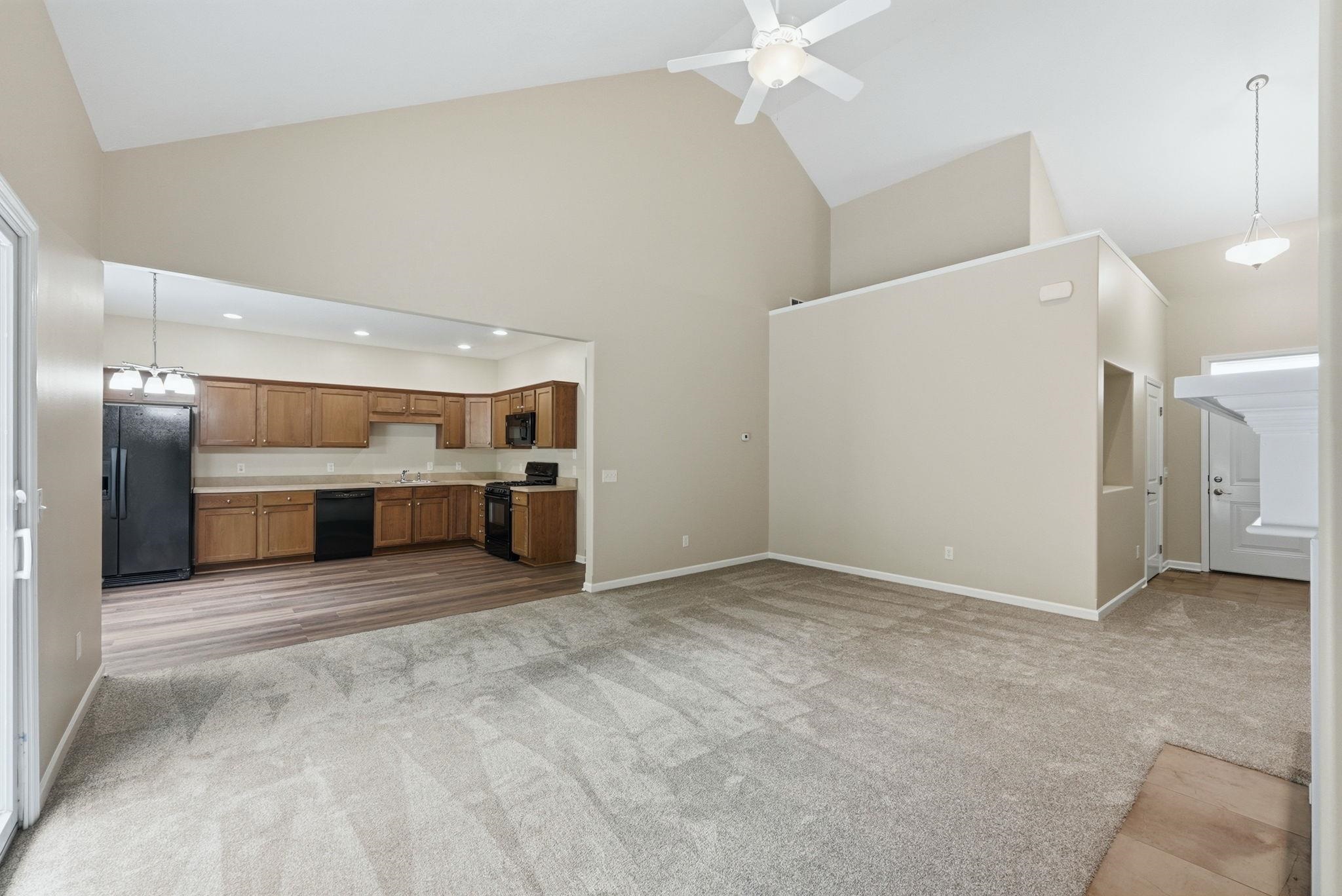 Open-concept living space featuring vaulted ceilings, a ceiling fan, and a kitchen with wood-finish cabinetry, black appliances, and durable countertops