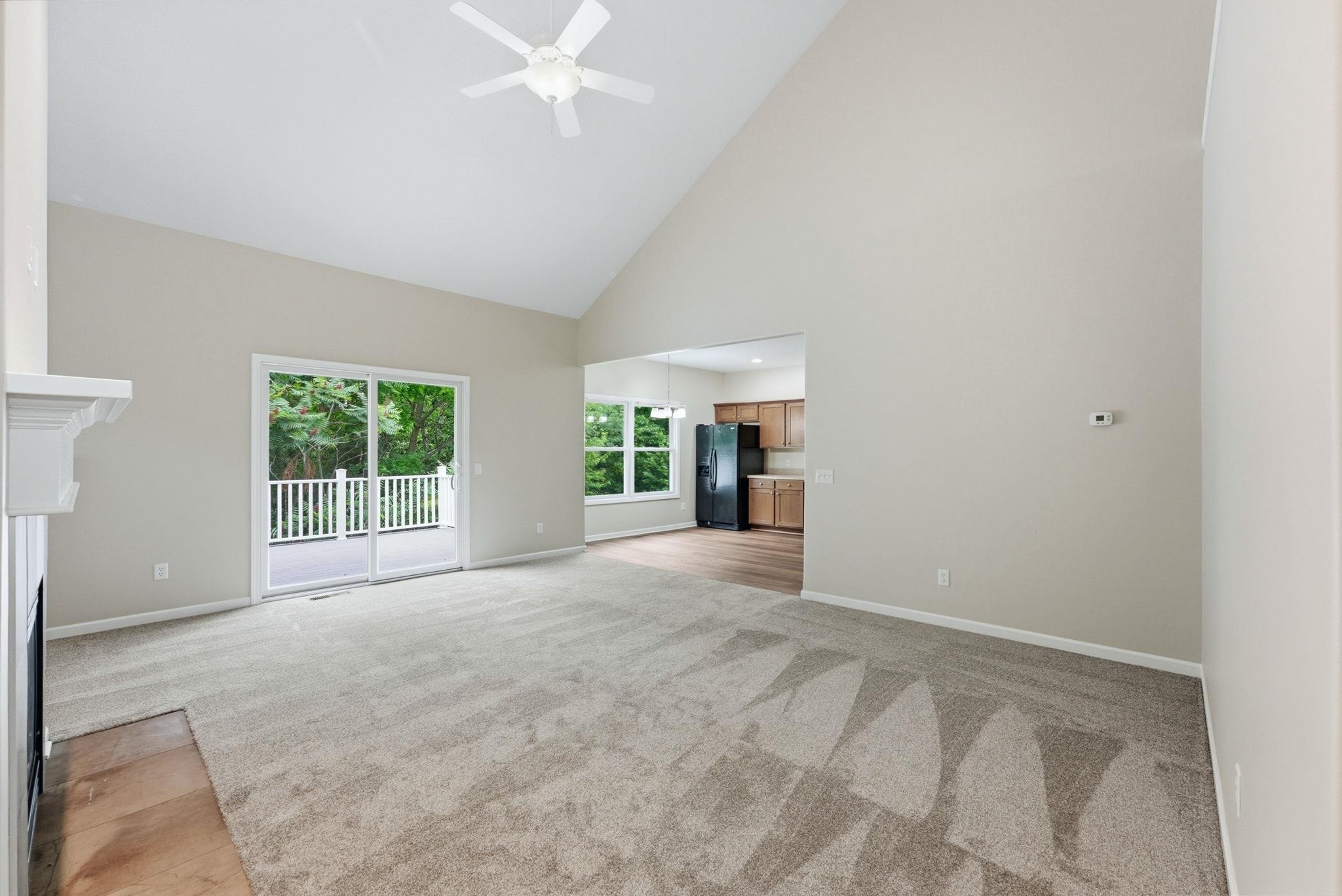 Spacious living area featuring a vaulted ceiling with a ceiling fan, a fireplace with a white mantle, and plush carpeting