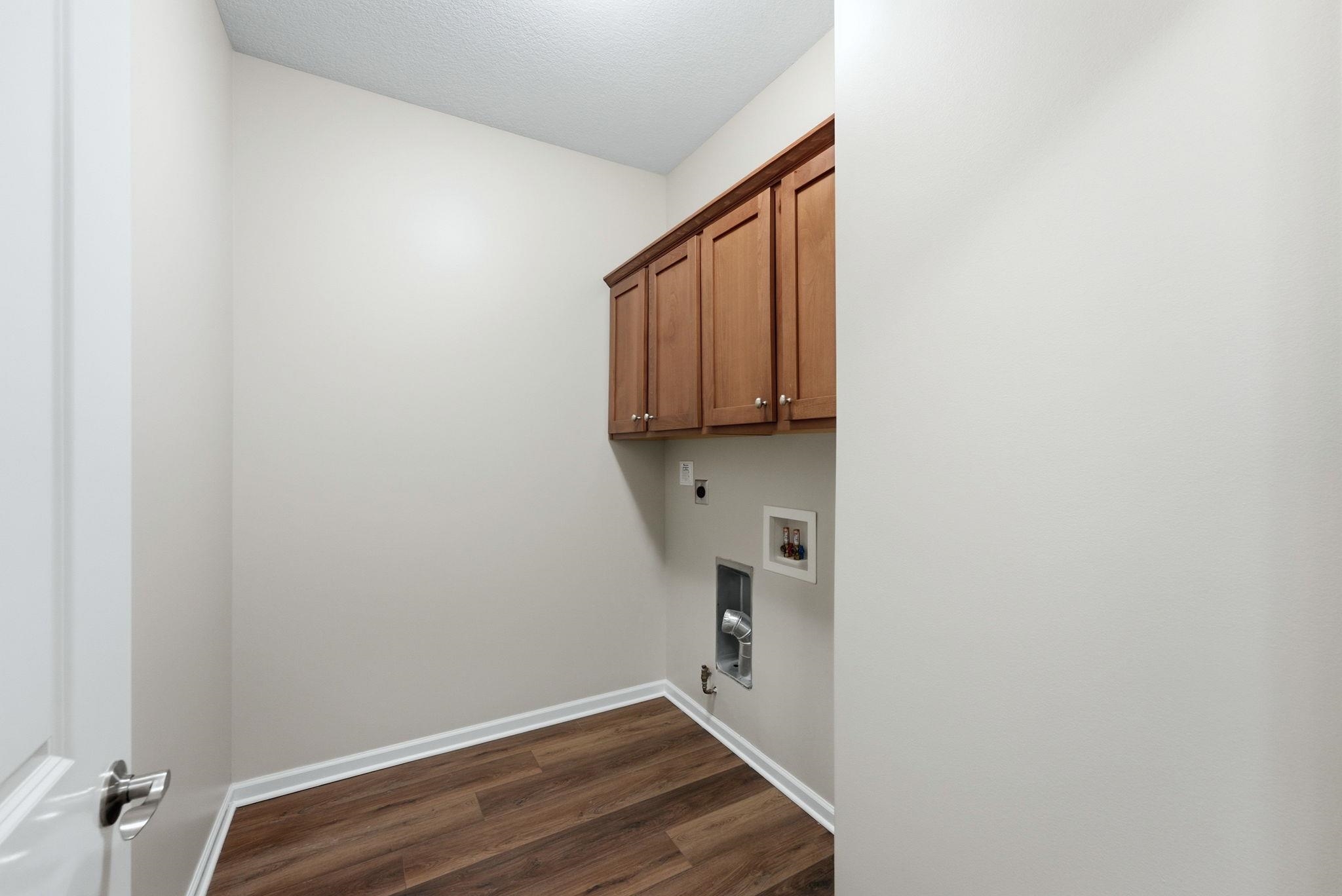 Dedicated utility area featuring wood-finish flooring, light neutral wall paint, and integrated wall cabinetry