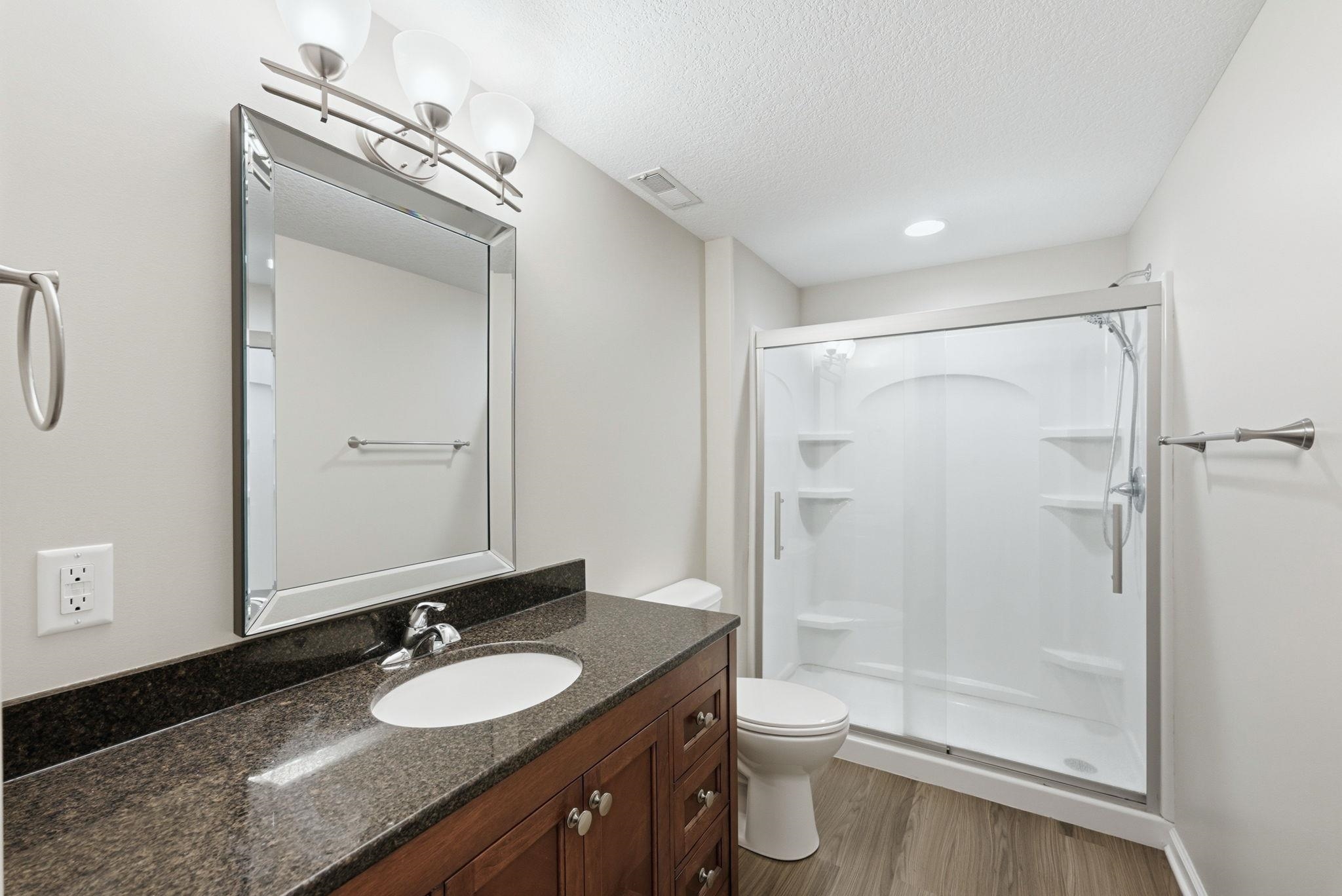 Bathroom featuring a dark wood-finish vanity with a dark speckled countertop, an undermount sink, and a framed mirror