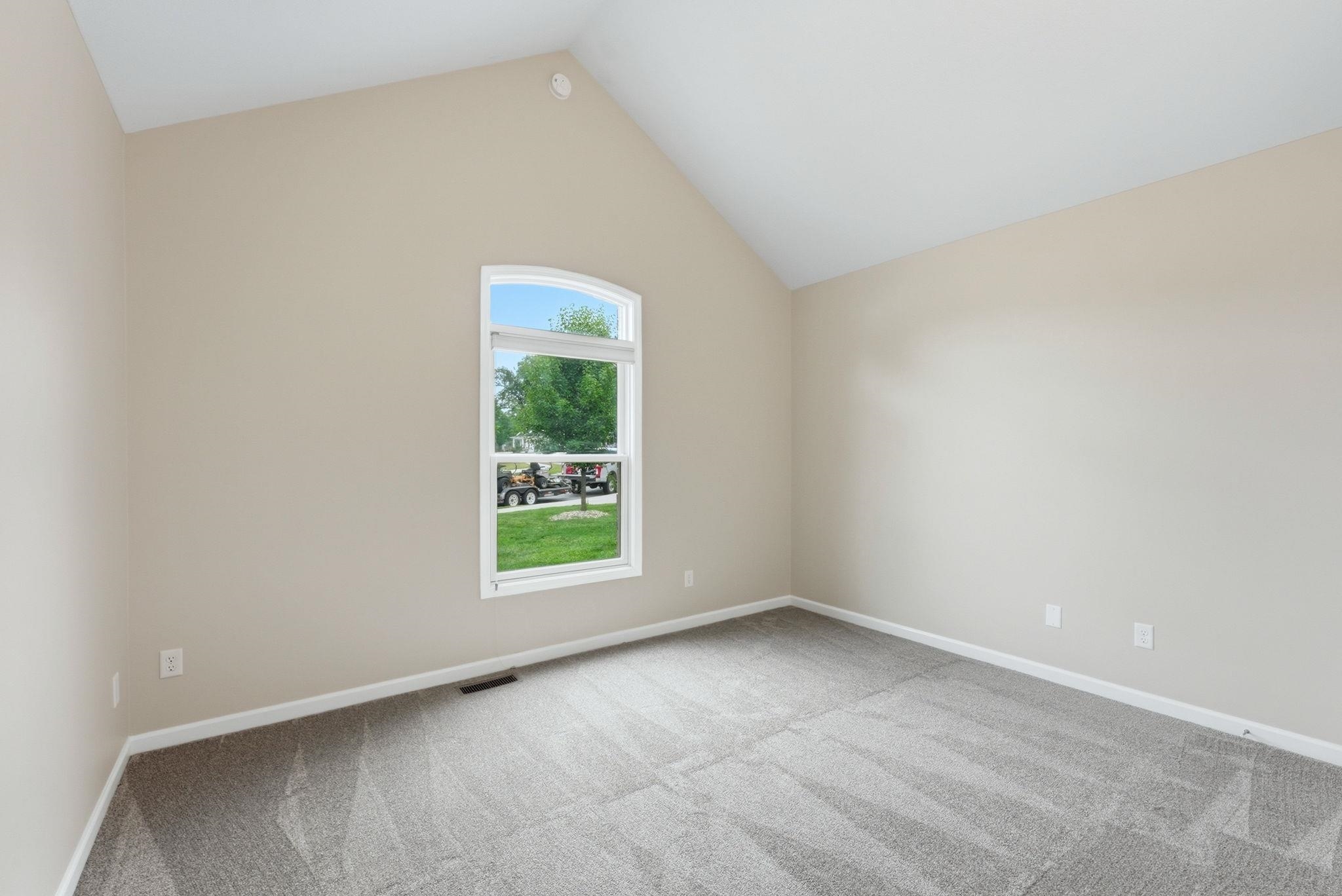 Vaulted ceiling room with an arched window, neutral wall paint, white trim, and grey carpet flooring
