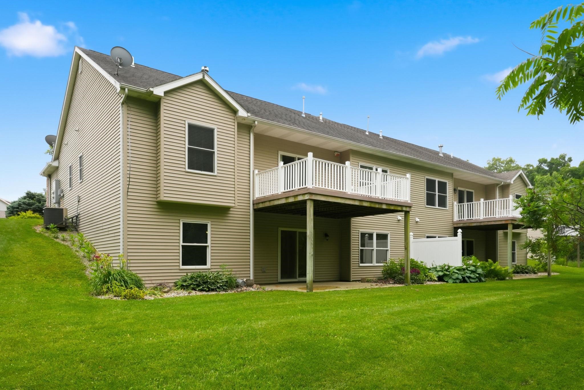 Rear exterior featuring multiple balconies with white railings, a ground-level patio, and light-colored siding