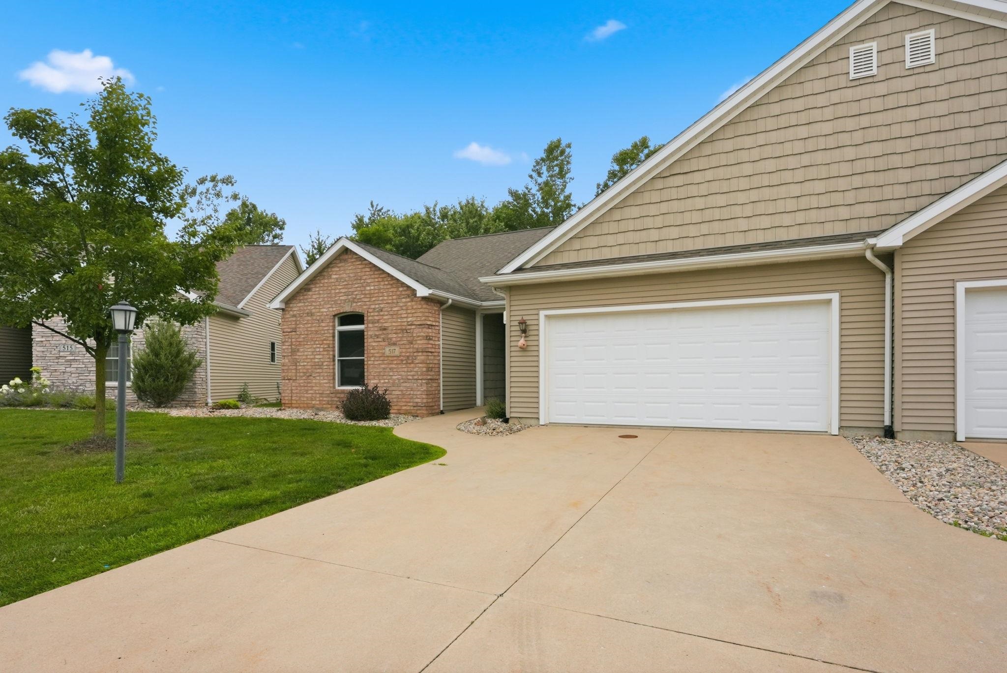 Exterior featuring a concrete driveway, two garage doors, horizontal siding, brick accents, and a landscaped yard with mature trees