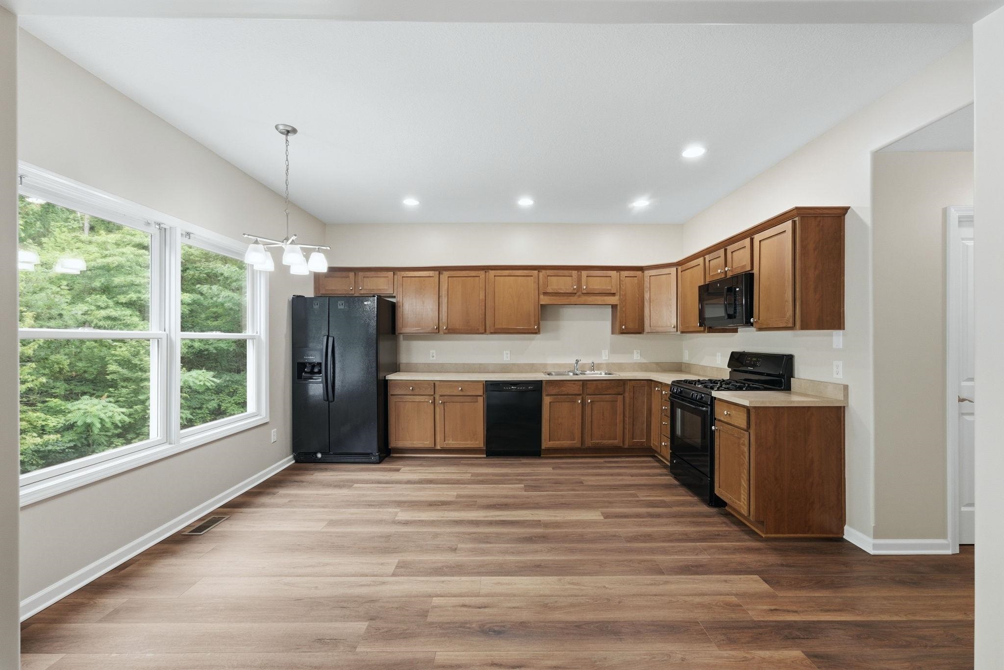 Kitchen featuring wood-finish flooring, ample natural light from large windows, recessed ceiling lights, and wooden cabinetry with black appliances