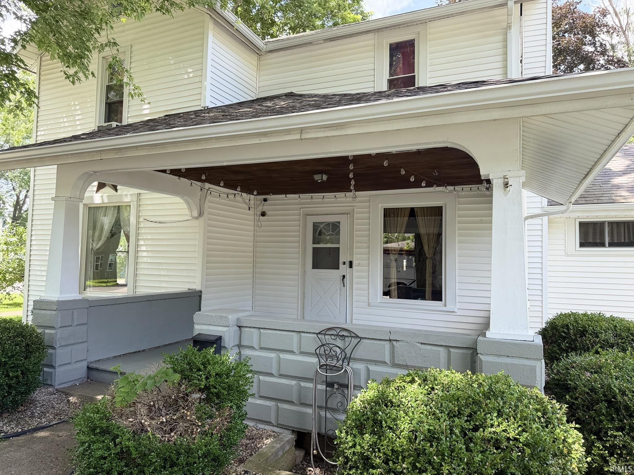Front porch entry featuring a wood-finish ceiling, white pillars, and a grey block foundation