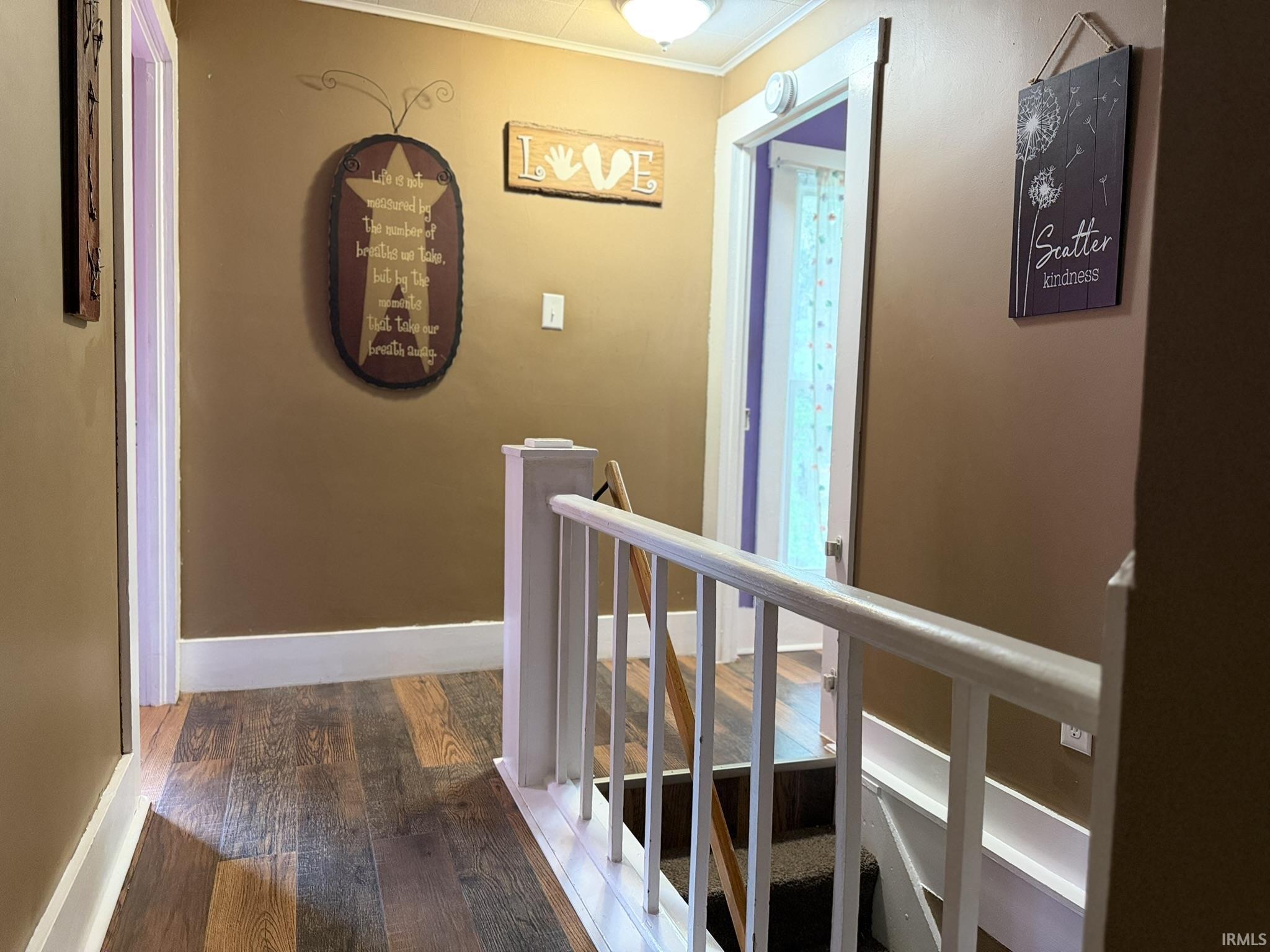 Hallway featuring wood-finish flooring, white trim, and a white balustrade leading to a carpeted staircase